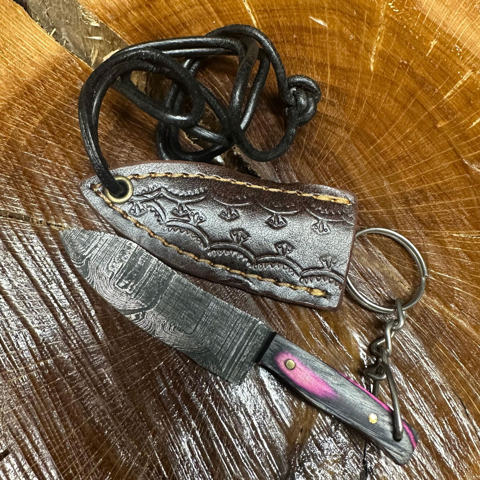 MHS Cutlery Keychain Blade Knife Pink Black With Leather Case Necklace R39: Small key chain-sized fixed-blade knife featuring a patterned steel blade and a compact epoxy-resin/wood pink/black-tone handle secured with brass pins. Includes a fitted brown leather sheath with
