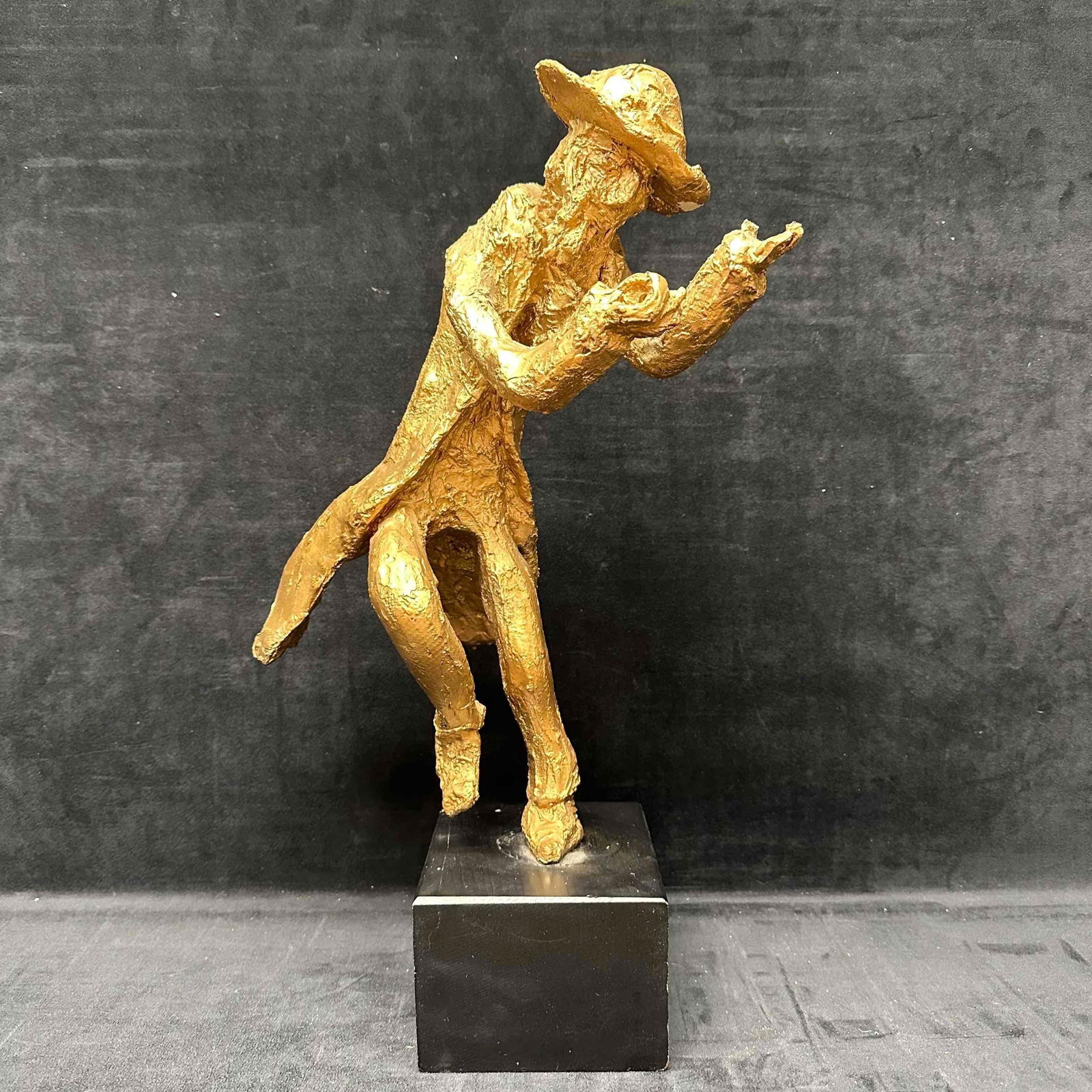 Modernist Resin Sculpture Golden Figure in Motion with Outstretched Hands on Wooden Base JB: This captivating modernist sculpture, cast in a radiant golden finish, depicts a dynamic figure frozen mid-stride, caught in the act of a compelling gesture. Poised on a sleek black wooden pedestal,