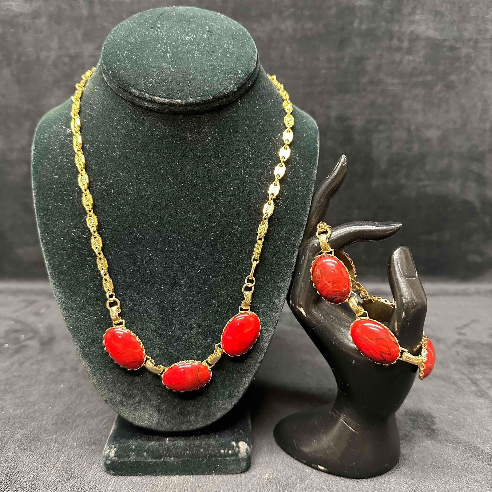 Gold-Tone Necklace and Bracelet Set with Red Cabochon Faux Red Stone Accent: Gold toned necklace and bracelet set with red blackish faux stone cabochon setting. No distinctive markings. These items are in good pre-owned, previously displayed condition with light wear, and