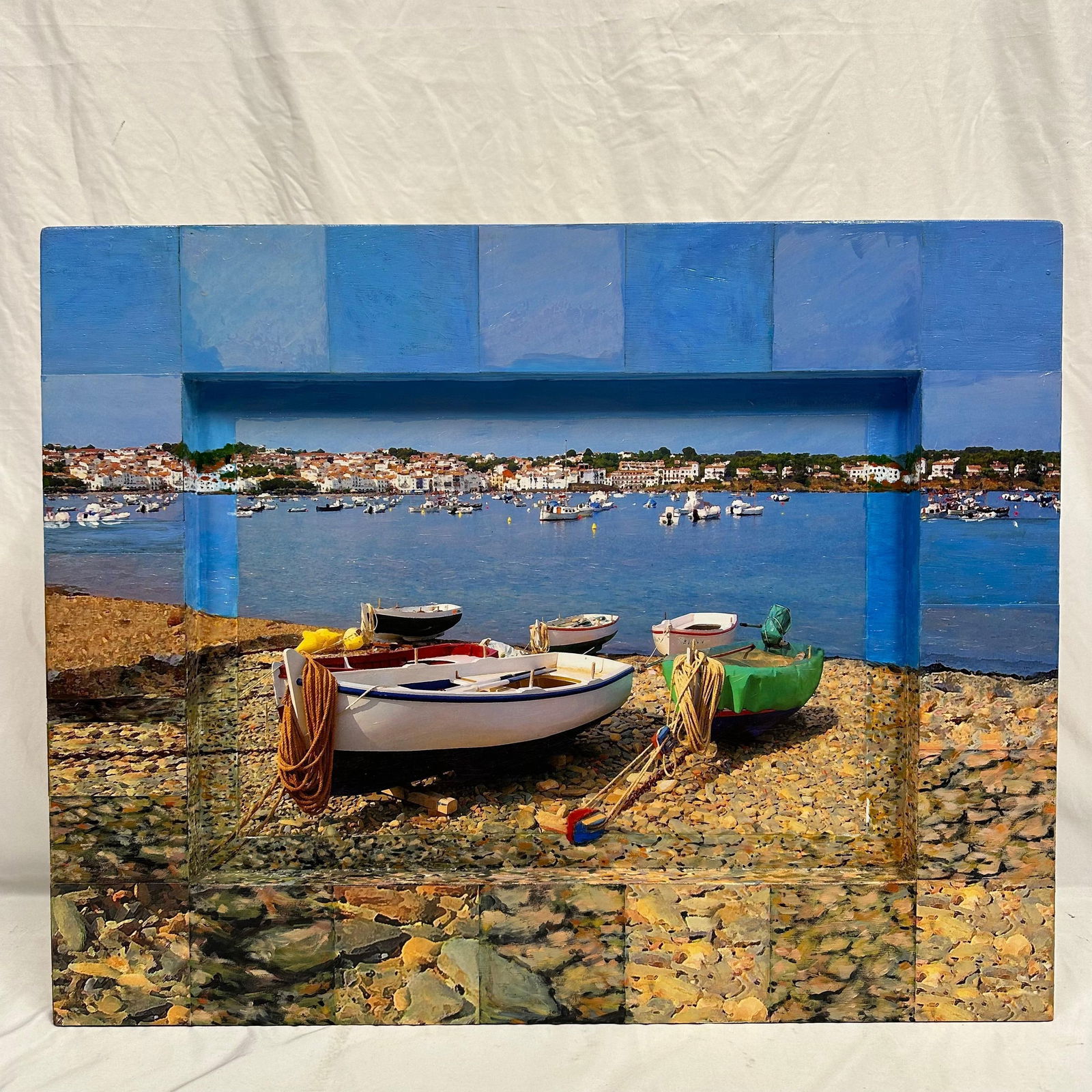 Robert Stein Mixed Media Relief Cadaques Boats Framed Wall Wood Artwork: Mixed media relief artwork by Robert Stein titled Cadaques Boats. The composition depicts small fishing boats resting on a rocky shoreline with a harbor and coastal village in the background, rendered
