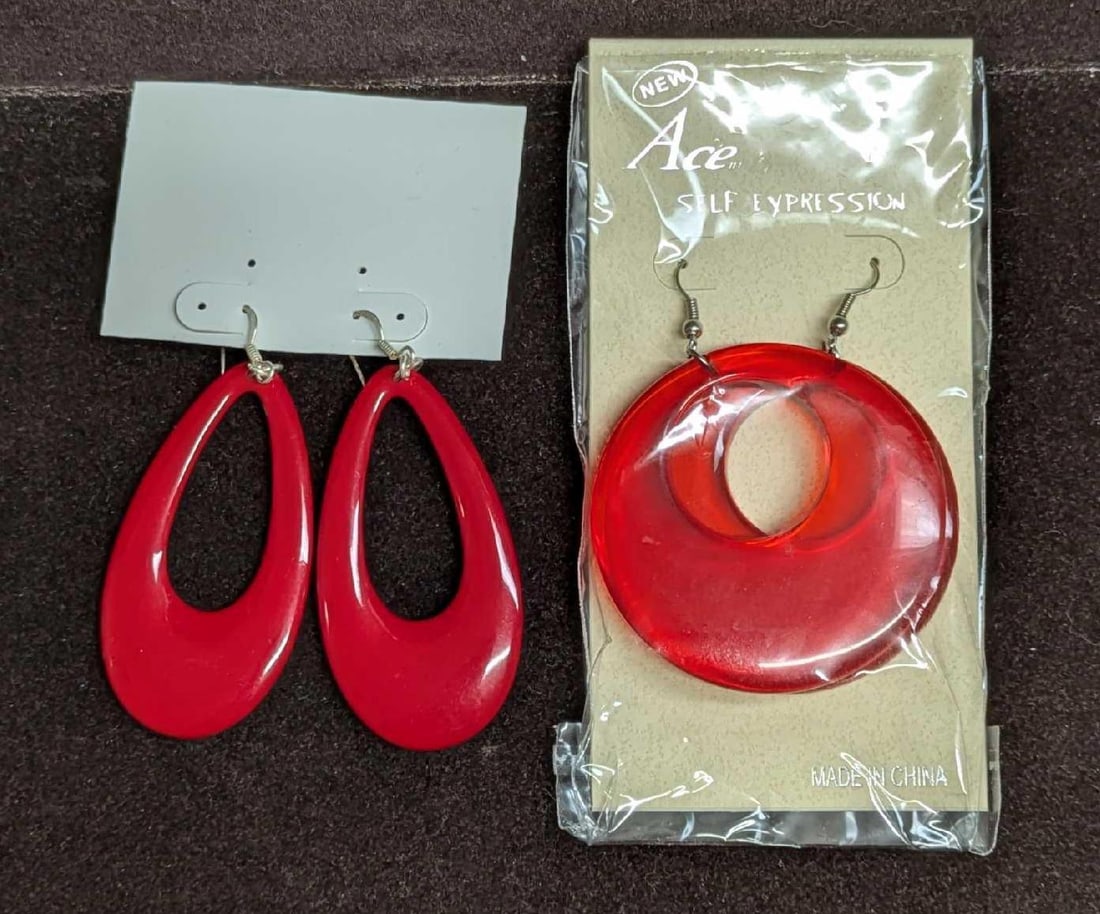 2 Set Of Red Plastic And Lucite Red Earrings: 2 Set Of Red Plastic And Lucite Red Earrings. This lot includes: (1) Set Of Sealed Opaque New Old Stock Hoop Earrings.Both come sealed in the original package that is approx 2 1/2" x 1/2" x