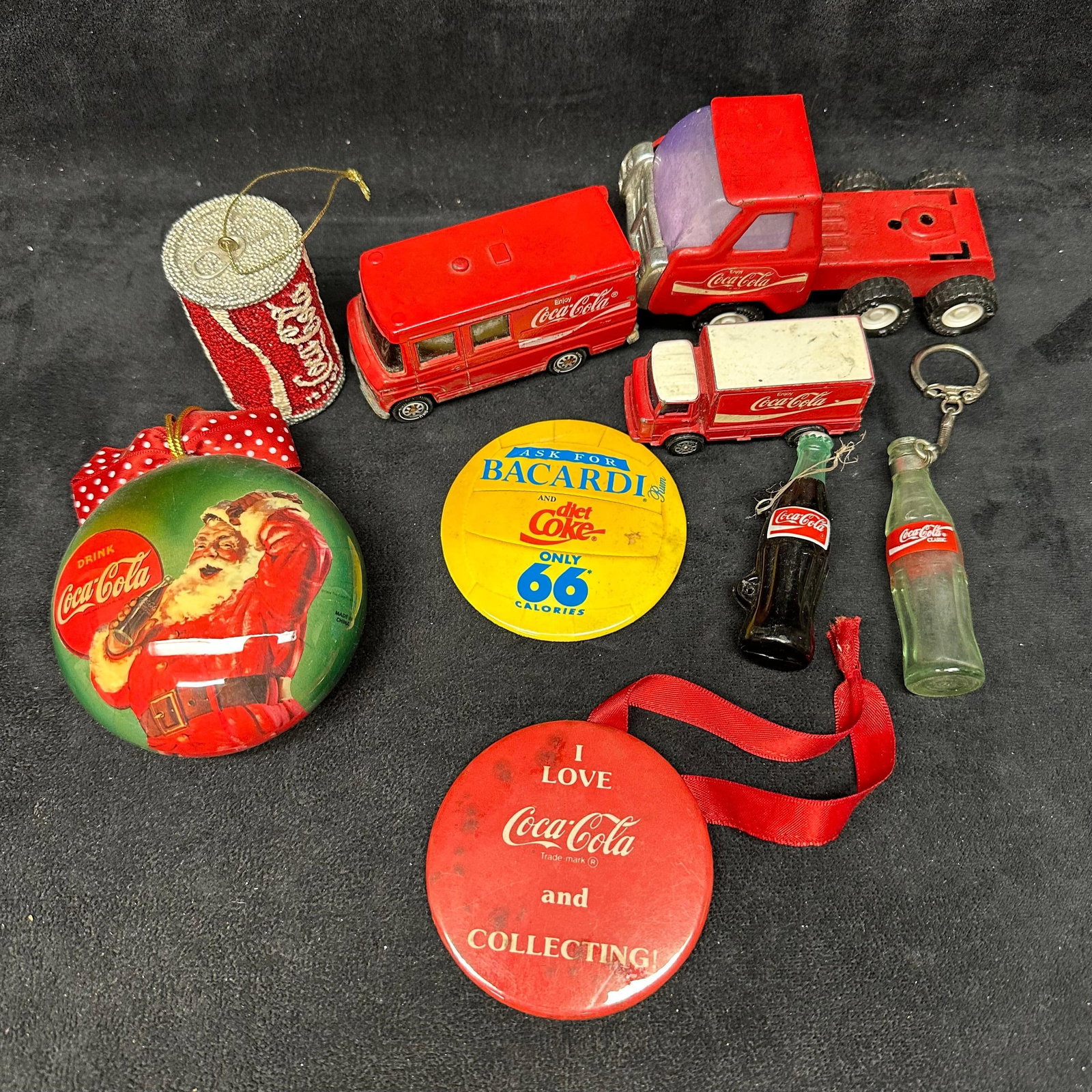 Group Lot of Coca-Cola Collectibles Toy Vehicles Ornaments Buttons and Mini Bottles: Mixed group of Coca-Cola themed collectibles, including die-cast and plastic delivery vehicles, Christmas ornaments, advertising pins/badges, miniature glass bottle items, and novelty accessories. The