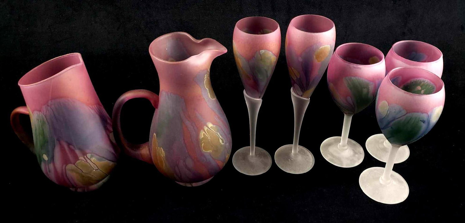 Lot of 7 Nouveau Art Glass by Rueven Glasses and Pitchers: Lot of 7 Nouveau Art Glass by Rueven Glasses and Pitchers. This set is in great condition overall. The lot contains: 1 art glass pitcher with ruffled edge. Measures 9.5" H x 7" W. 2 art glass