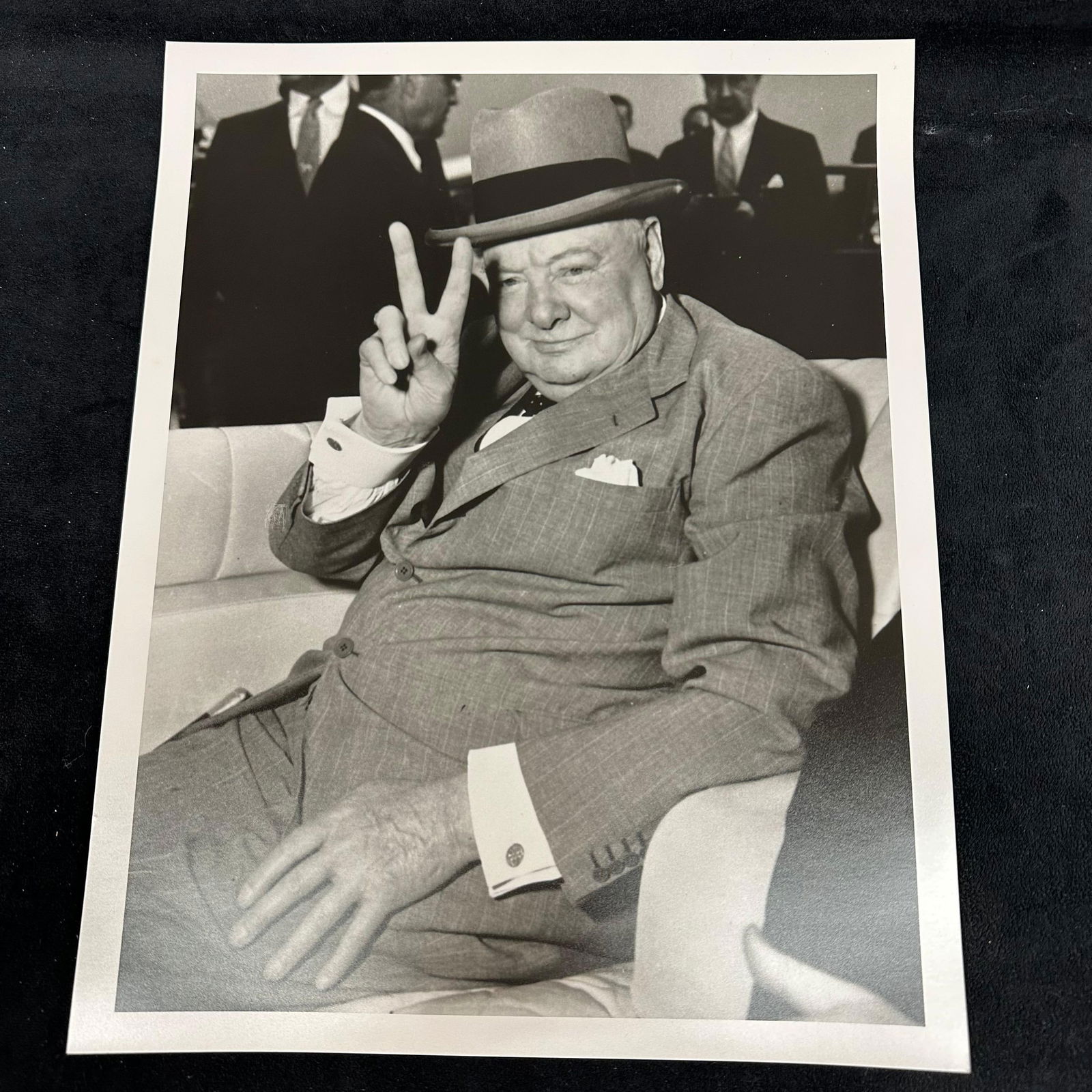Analog Photo Print of Winston Churchill V for Victory Pose Black and White: An analog black-and-white photo print depicting Winston Churchill giving his iconic “V for Victory” hand gesture. Churchill is shown seated in a suit and hat, exuding his characteristic