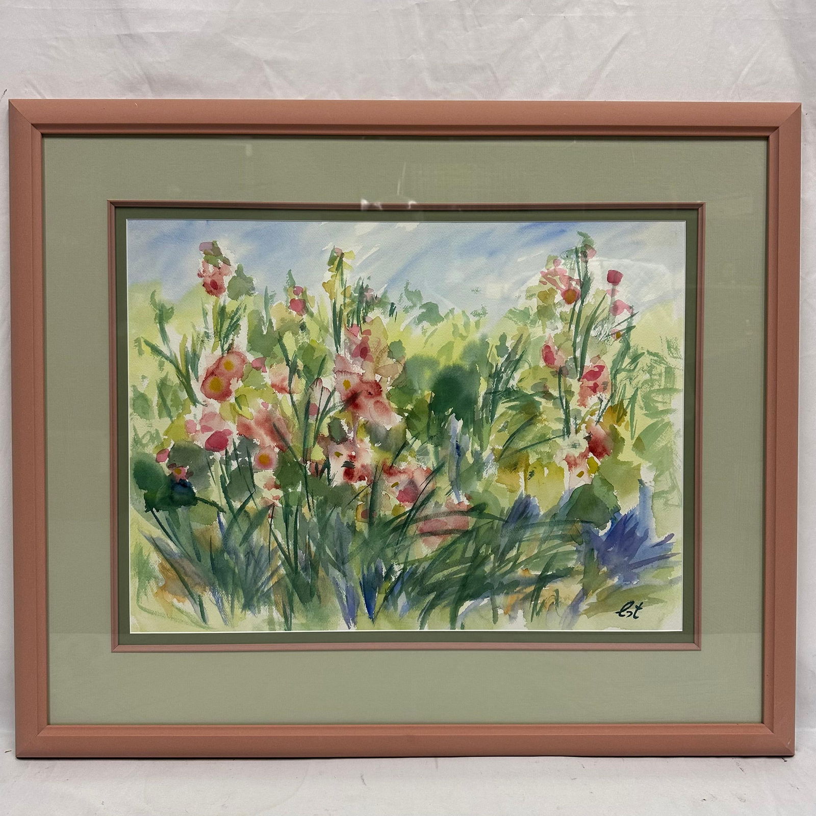 Framed Watercolor Floral Garden Scene Signed Est Pink Frame: Framed watercolor painting depicting a vibrant garden scene with pink wildflowers and lush green foliage. Signed, Est, at the lower right. Housed in a double-matted pink frame with glass. Artwork