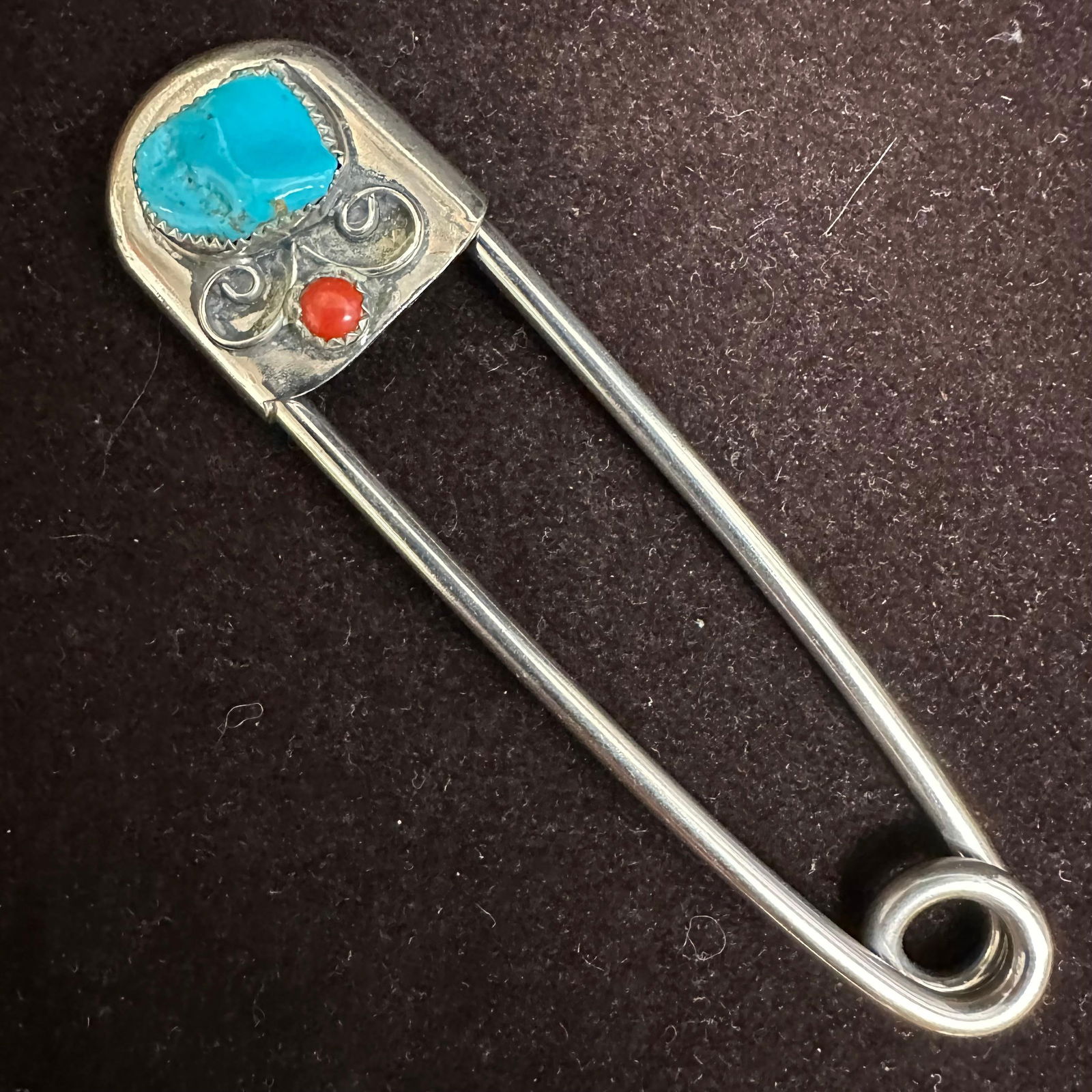 Artisan Turquoise and Coral Safety Pin Style Brooch Silver Tone Metal: Appears to be a handmade safety pin–style brooch featuring a large irregular turquoise cabochon set at the head, accented with a small round red coral or carnelian stone. Decorative scrollwork surro