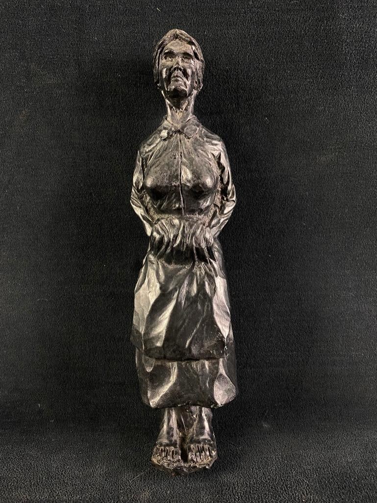 Black Resin Statue of a Woman: Black Resin Statue of a Woman Cast black resin statue of a woman in 19th century clothes. Shows her standing, with her hands in her apron. The feet appear to have been broken off and repaired at