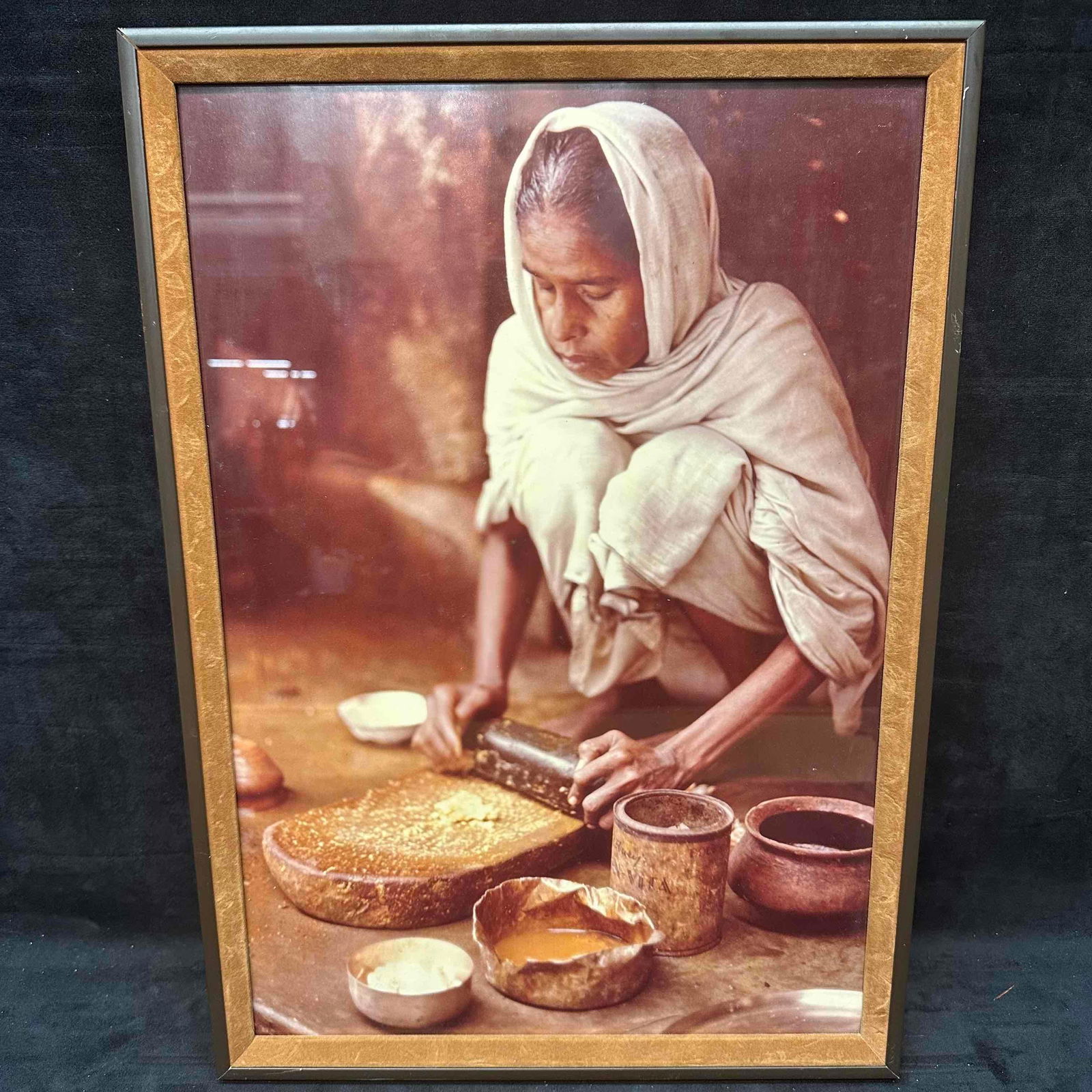 Framed Photograph Woman Preparing Food Cultural Print Poster: Framed photograph print poster depicting a woman preparing food using traditional methods. The image captures rich earthy tones and authentic cultural detail, showing various bowls, utensils, and text