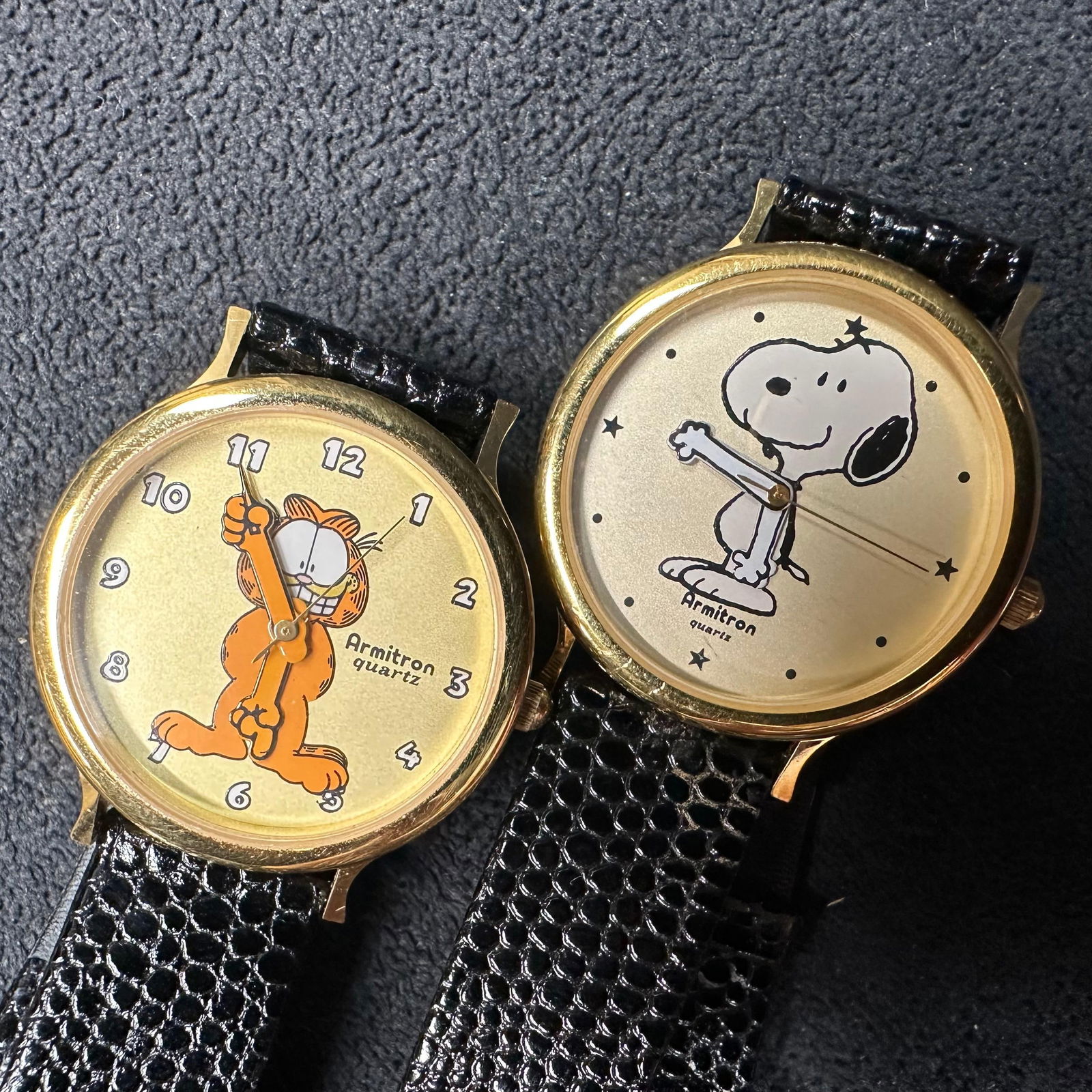 Pair of Vintage Armitron Quartz Character Watches Garfield and Snoopy Leather Band: Pair of vintage Armitron quartz wristwatches featuring classic cartoon characters Garfield and Snoopy. Both watches have gold-tone base metal bezels with stainless steel backs and black genuine