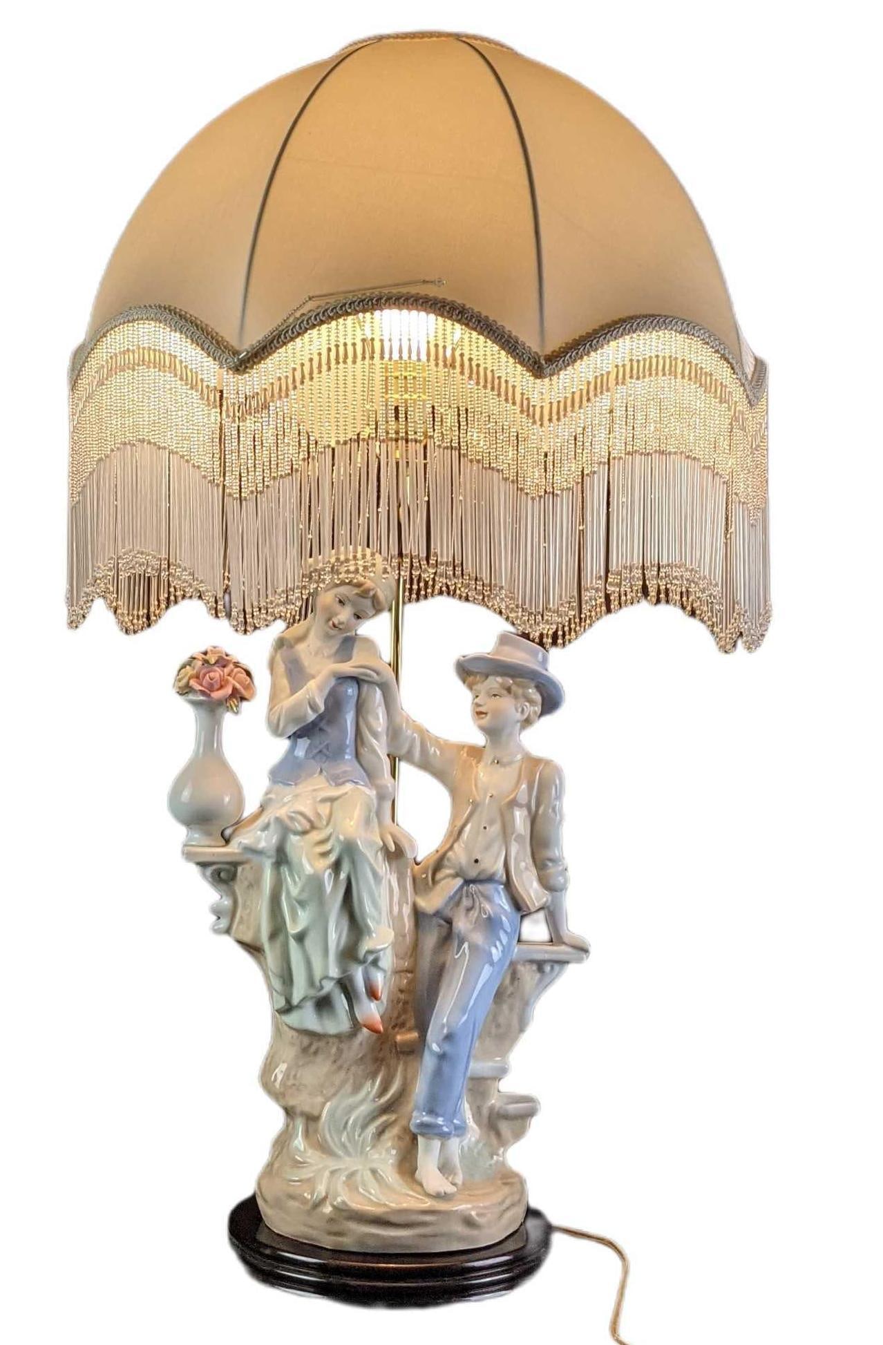Similar To Lladro Boy And Girl Porcelain Umbrella Lamp: This very unique Porcelain lamp shows two young teens as they avoid the rain under a rather large umbrella. They sit upon an old wall with a vase and wait for the rain to finish. This resembles a Llad