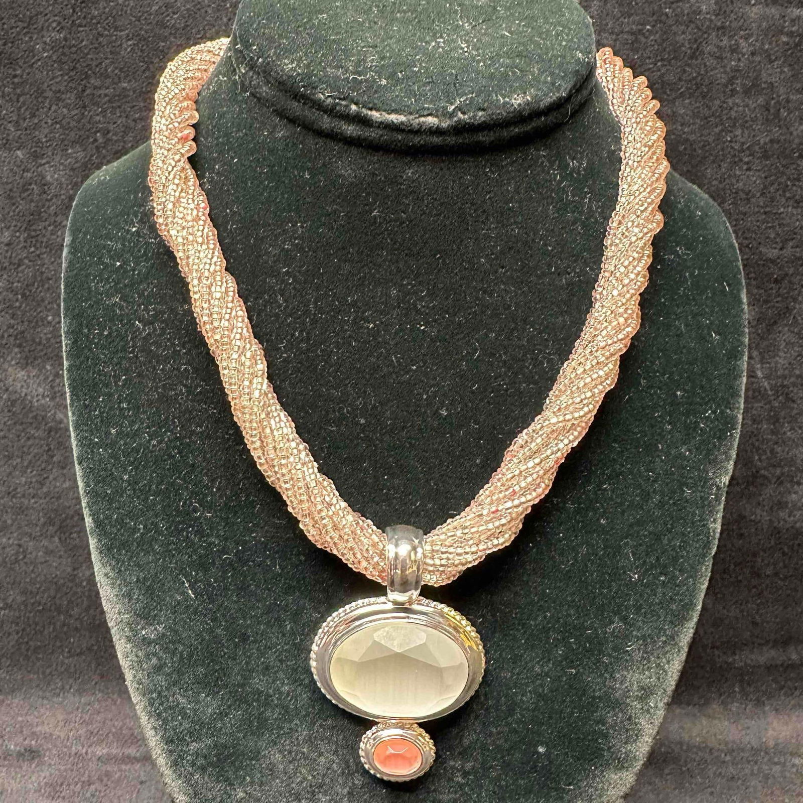 Twisted Pink Beaded Necklace with Faceted Glass and Coral-Tone Double Pendant: This elegant twisted pink seed bead necklace featuring a bold double-drop pendant. The top pendant showcases a large faceted clear glass center framed in silver-tone metal, accented below with a