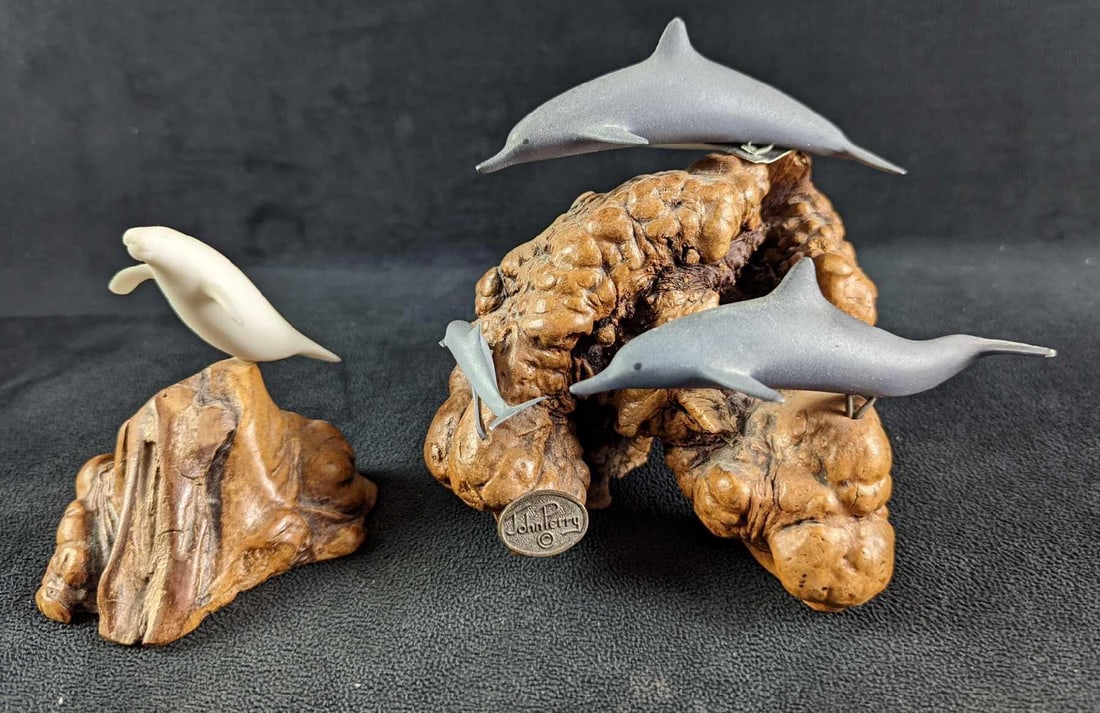 John Perry Dolphin & Manatee Sculptures Burl Wood Driftwood: This lot includes: (1) Manatee. This is approx 4" x 2 1/2" x 3 3/4".(1) Dolphin Family. This is approx 5" x 5" x 5 1/2". The dolphins have chips and the baby is missing a fin.