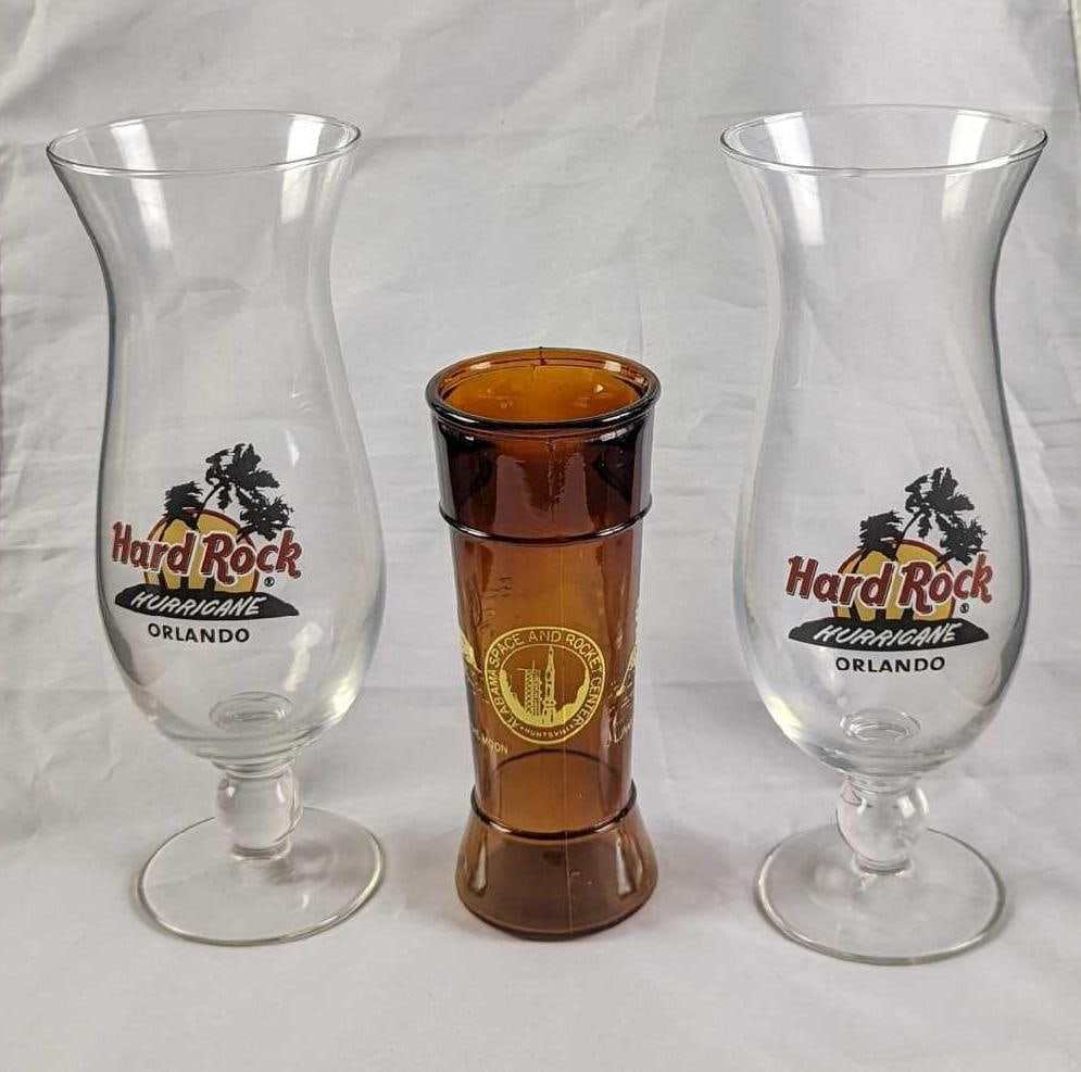 2 Hard Rock Orlando Hurricane Glasses & Alabama Space & Rocket Center Tumbler: This lot consists of: (2) Hard Rock Orlando Hurricane Glasses. Each is approx 3" x 3" x 9 1/4" and together they weigh 1.66lb.(1) Alabama Space & Rocket Center "First Man On The