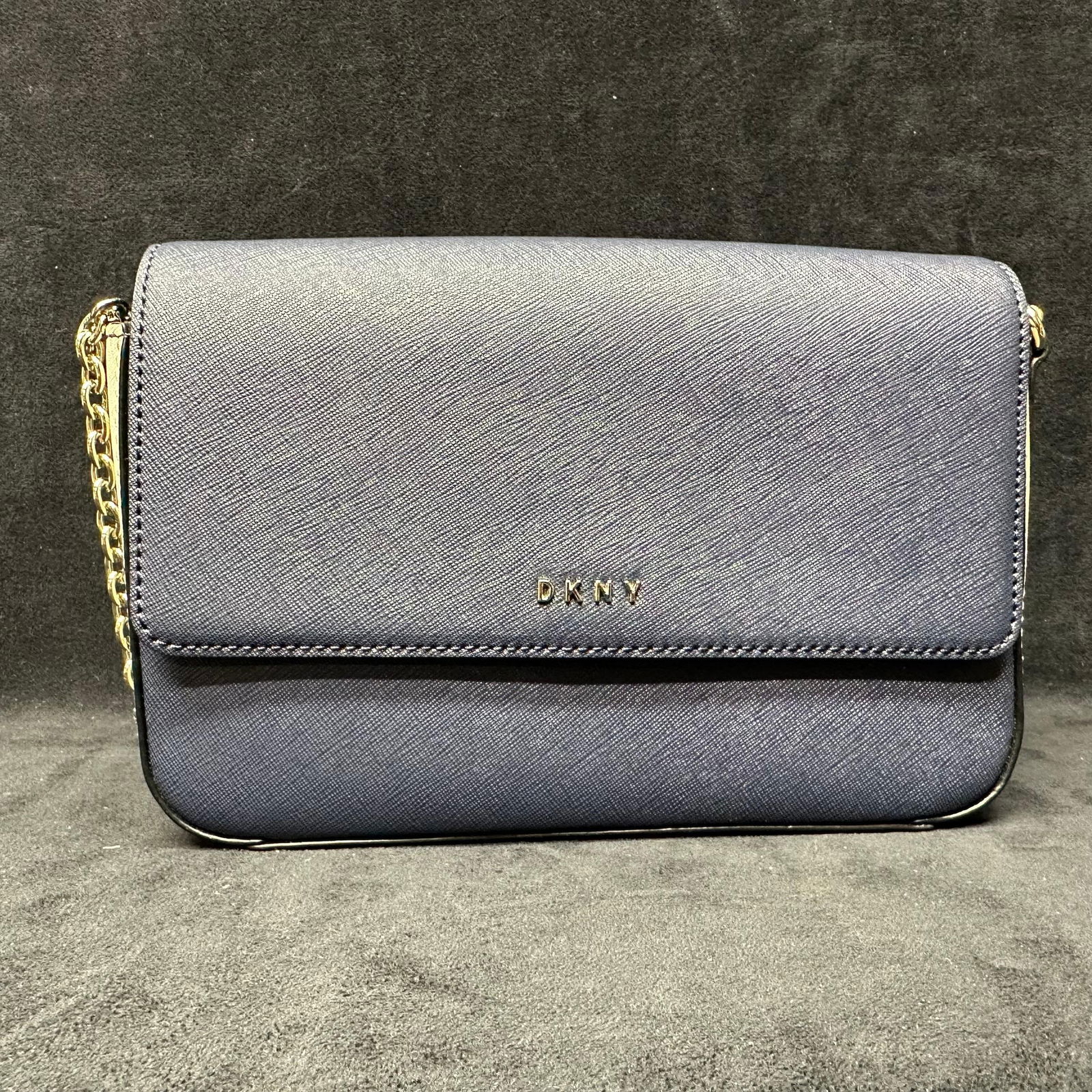 DKNY Navy Blue Saffiano Style Leather Crossbody Bag with Chain Strap: Donna Karan New York DKNY navy blue small crossbody handbag crafted in textured saffiano-style leather. Features a structured flap-front design with gold-tone DKNY logo, magnetic snap closure, and a