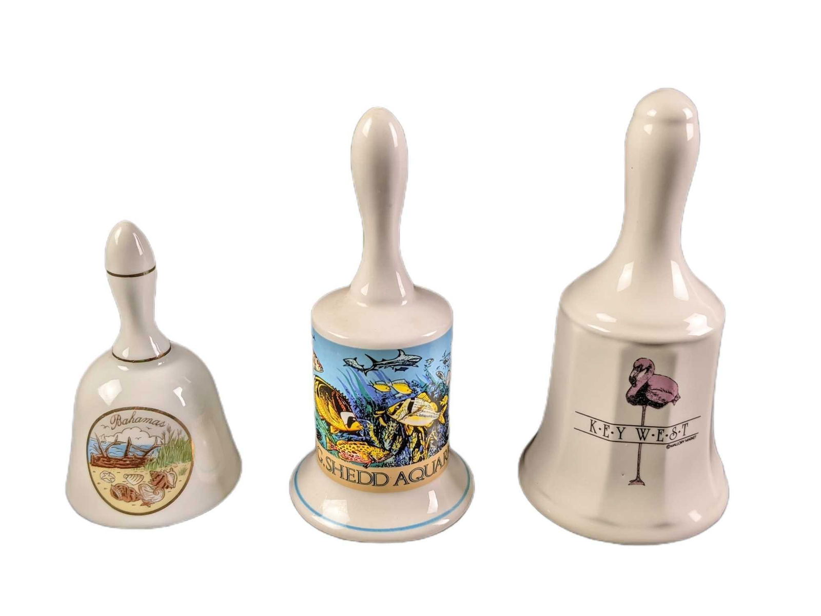 3 Vintage Porcelain Souvenir Bells Florida Key West Aquarium: This lot includes: (1) Key West Flamingo Bell. This is approx 3" x 3" x 5 1/2".(1) John G.Shedd Aquarium, Chicago. This is approx 2 1/2" x 2 1/2" x 5 1/2"(1) Bahamas Bell.