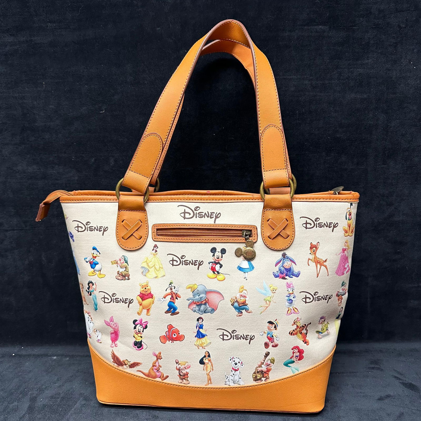 Ardleigh Elliott Ultimate Disney Classic Carryall Tote Bag Mickey Mouse: Canvas and faux-leather Disney tote featuring an all-over print of classic characters including Mickey, Minnie, Donald, Goofy, Winnie the Pooh, Dumbo, Bambi, Ariel, and others. Tan vegan-leather handl
