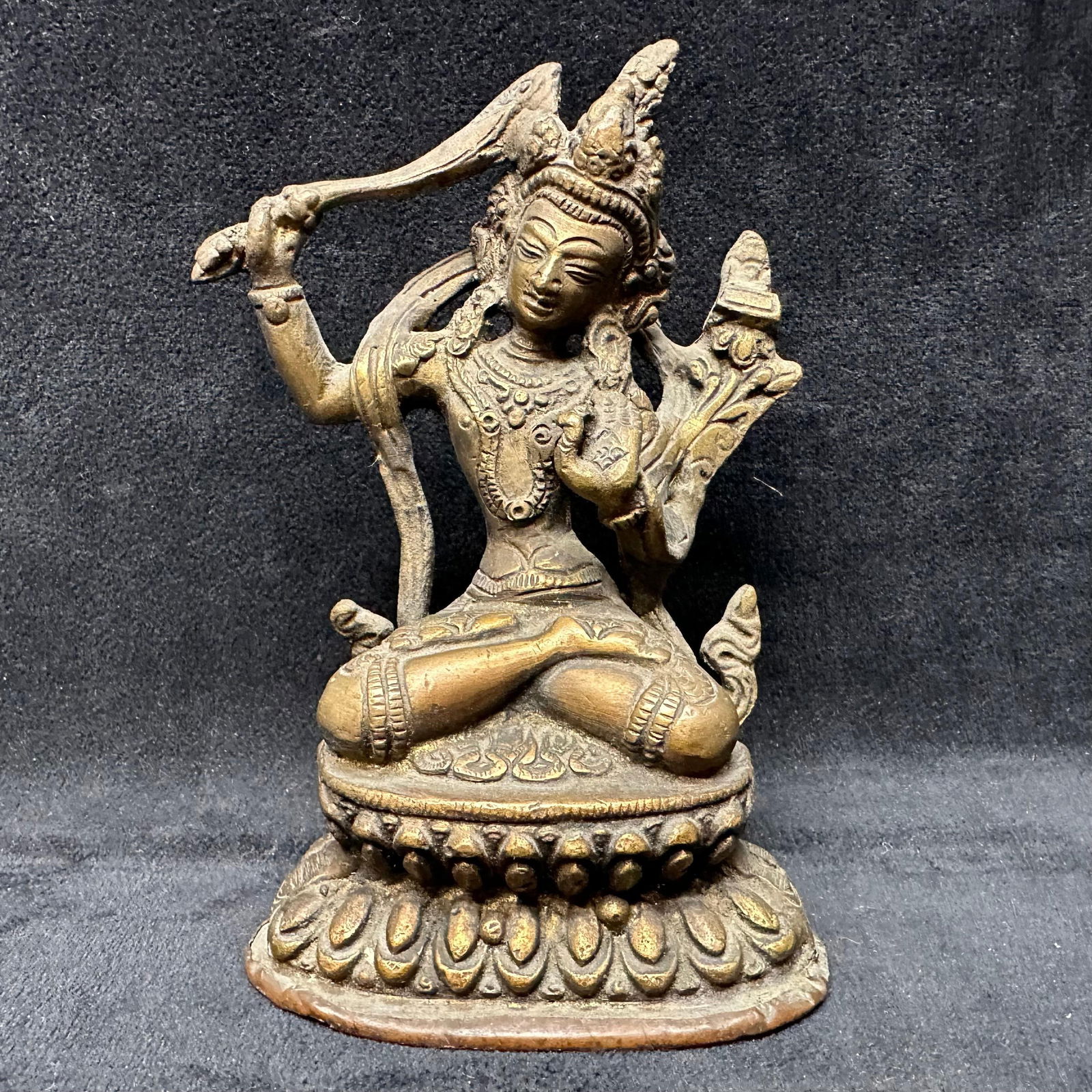 Antique Style Cast Bronze Tibetan Buddhist Deity Figure on Lotus Base: Cast bronze figure depicting a Tibetan Buddhist deity shown seated on a lotus pedestal in a dynamic pose, holding ritual attributes. The figure features detailed facial expression, elaborate