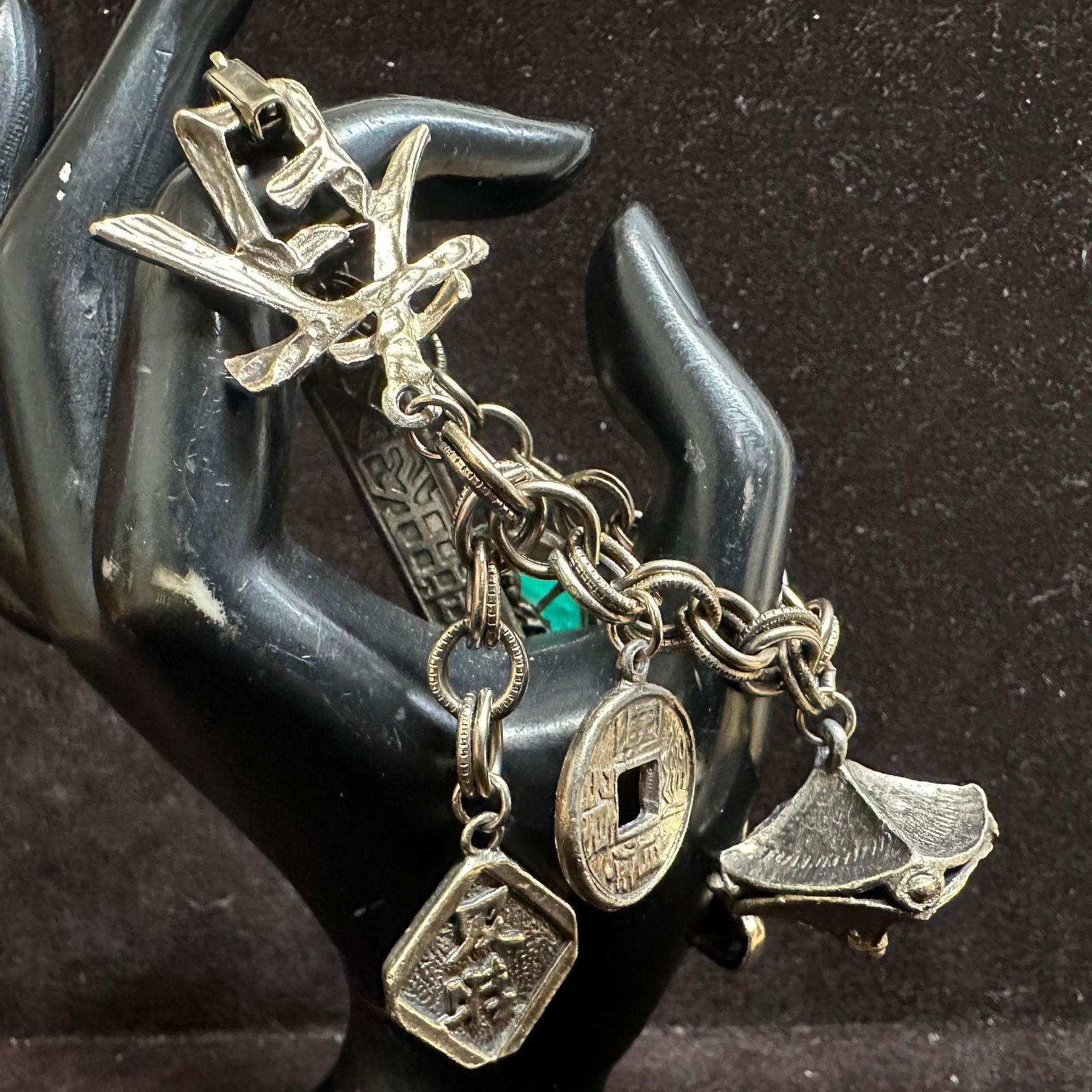 Asian Themed Charm Bracelet with Buddha Pagoda and Carved Green Stone: Heavy charm bracelet featuring multiple Asian-inspired charms attached to a chunky linked chain. Charms include a seated Buddha figure, pagoda-style temple, dragonfly motif, square-holed Chinese coin,
