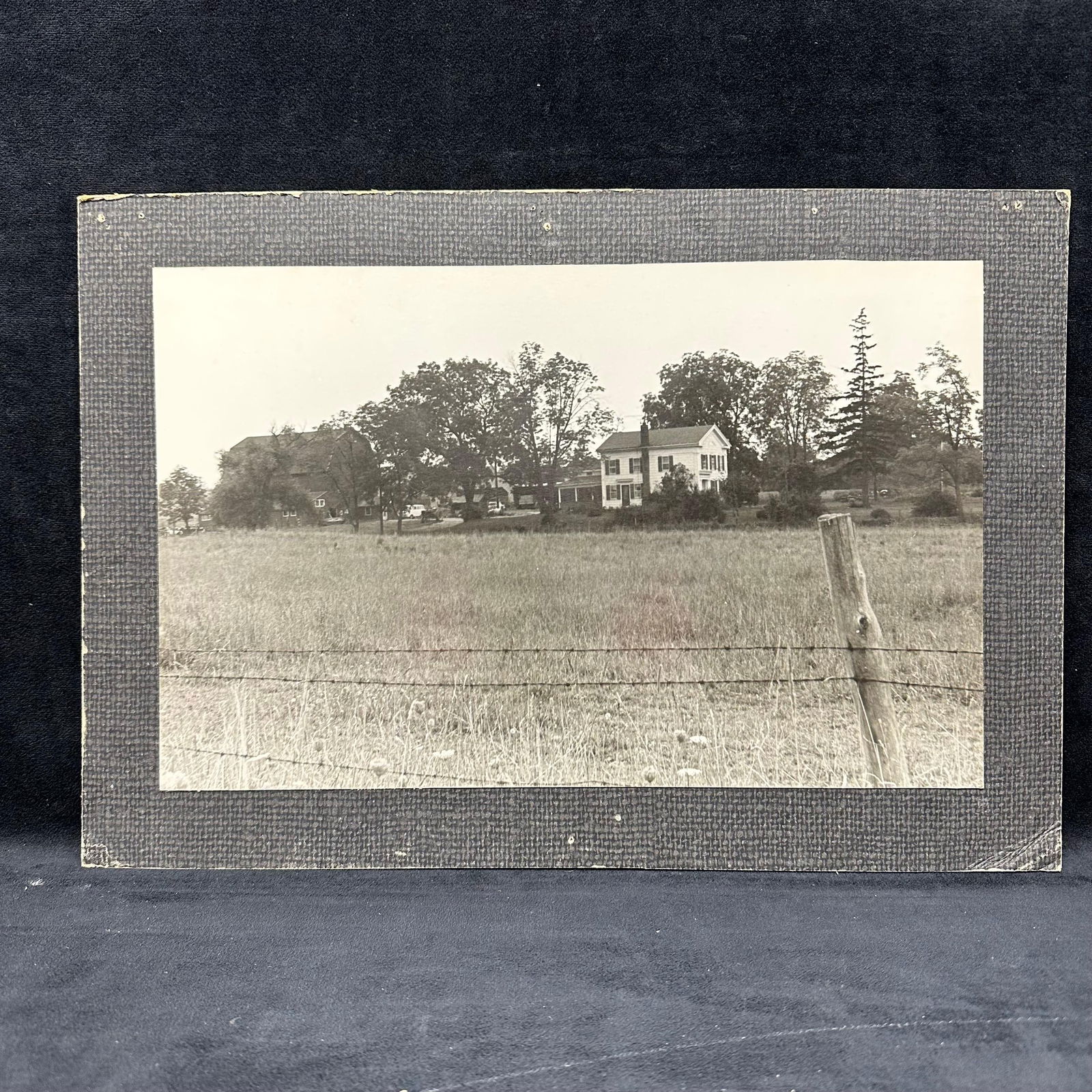 Vintage Silver Gelatin Photograph of Rural Farmstead Landscape: Vintage black and white silver gelatin photograph depicting a rural farmstead scene with a farmhouse, barn, trees, and open pastureland in the foreground. The composition shows a field with a barbed w