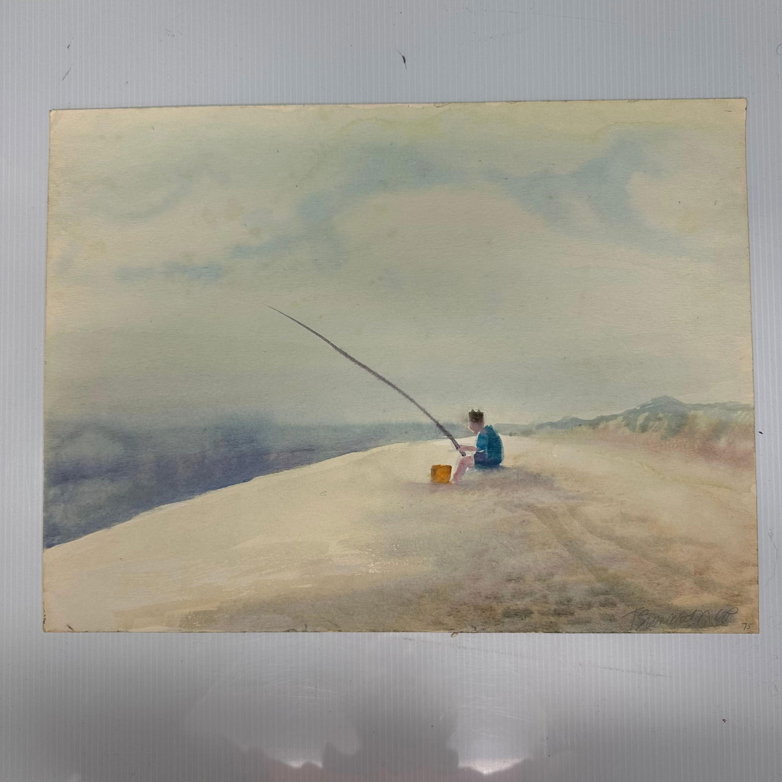 Dated 1975 Signed Coastal Fishing Scene Watercolor Painting: Original watercolor painting on paper depicting a solitary figure fishing along a sandy shoreline with ocean waves to the left and dunes in the background. Executed in soft washes with minimal