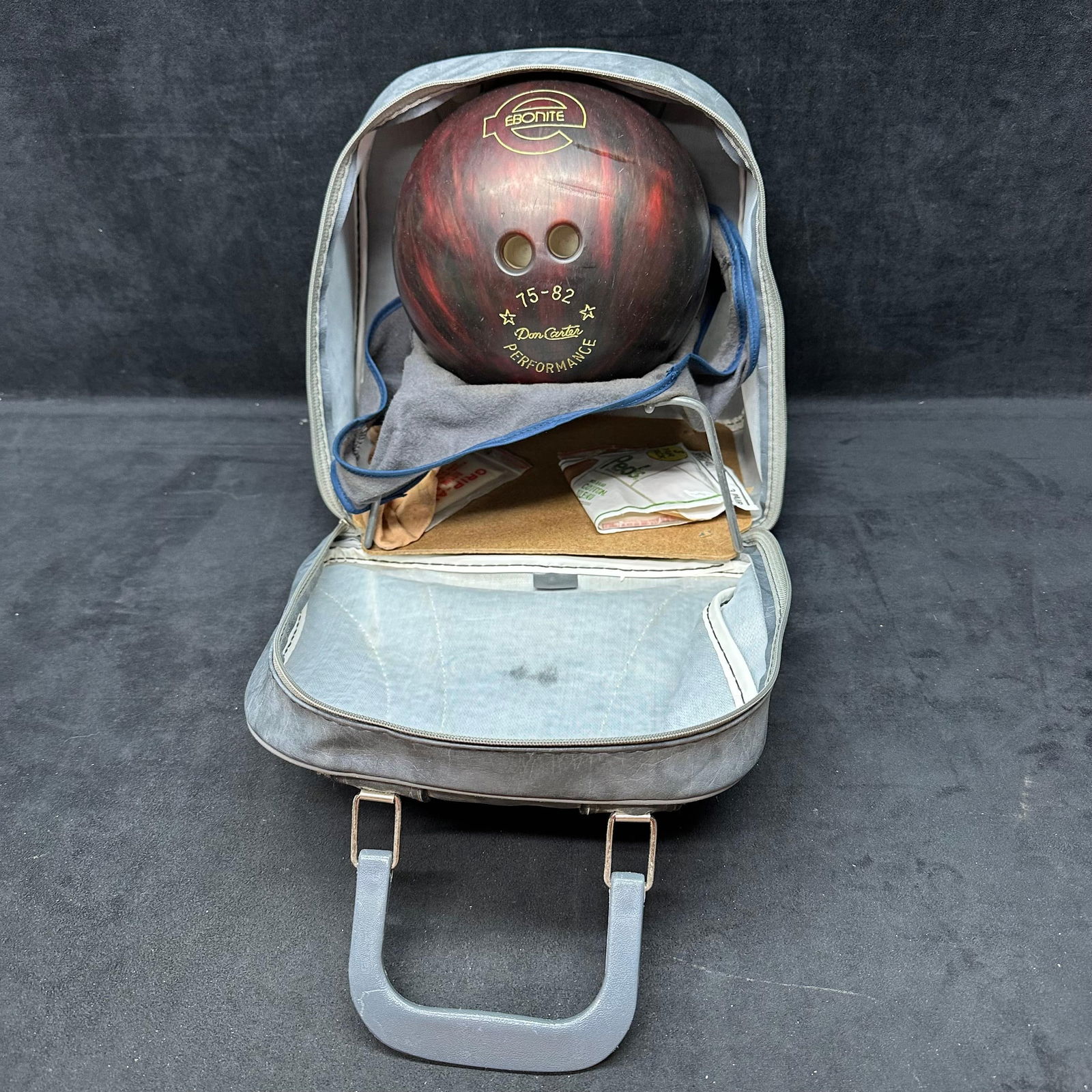 Ebonite Don Carter Performance Bowling Ball with Brunswick Carrying Case: Vintage Ebonite Don Carter Performance bowling ball, marked 75-82 with Ebonite logo. Marbled red, black, and brown finish with three drilled finger holes. Includes a vintage Brunswick gray bowling