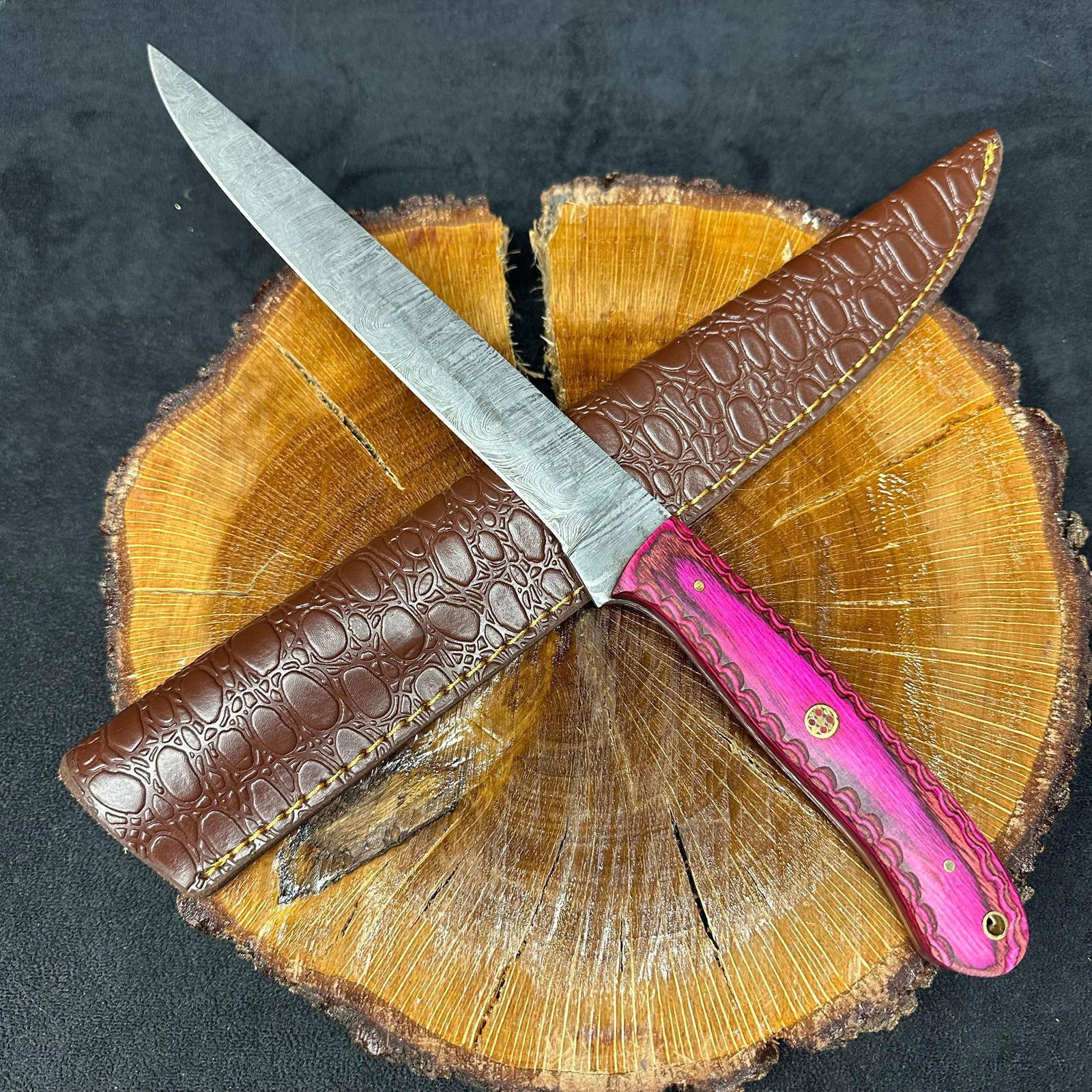Long Steel Straight Edge Knife with Pink Pattern Handle Q31: A custom knife featuring a patterned steel blade with a hammered finish and straight spine detail. The handle is constructed from a contoured, pink-patterned epoxy resin/wood composite material, secur
