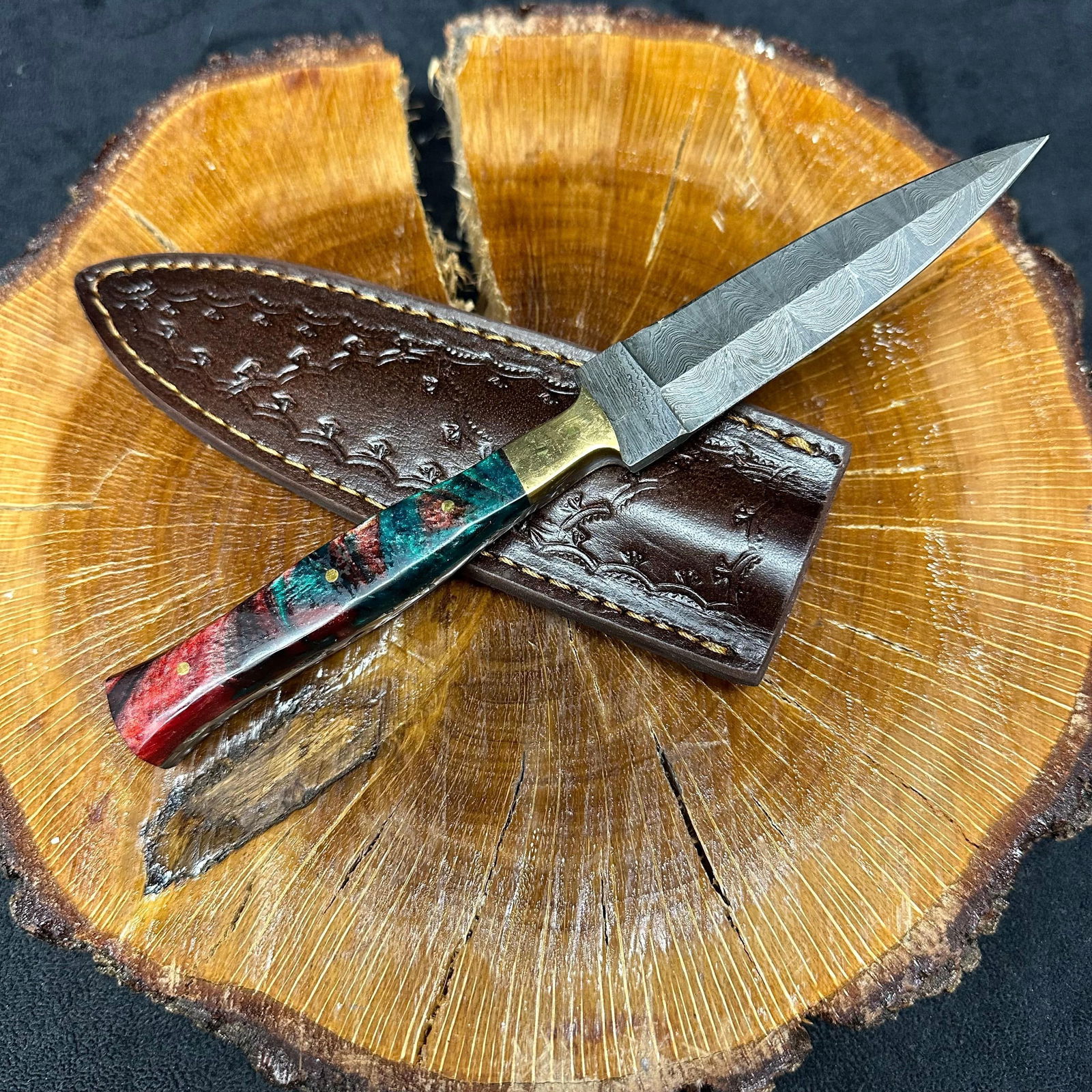 Fixed Blade Knife Spear Point Dagger Style MHS Cutlery Q23 Red Colored Handle: Fixed dagger-style blade knife by MHS Cutlery featuring a layered patterned steel blade and decorative spine work. The handle has a contoured, multi-colored wood/epoxy resin-style grip with metal mosa
