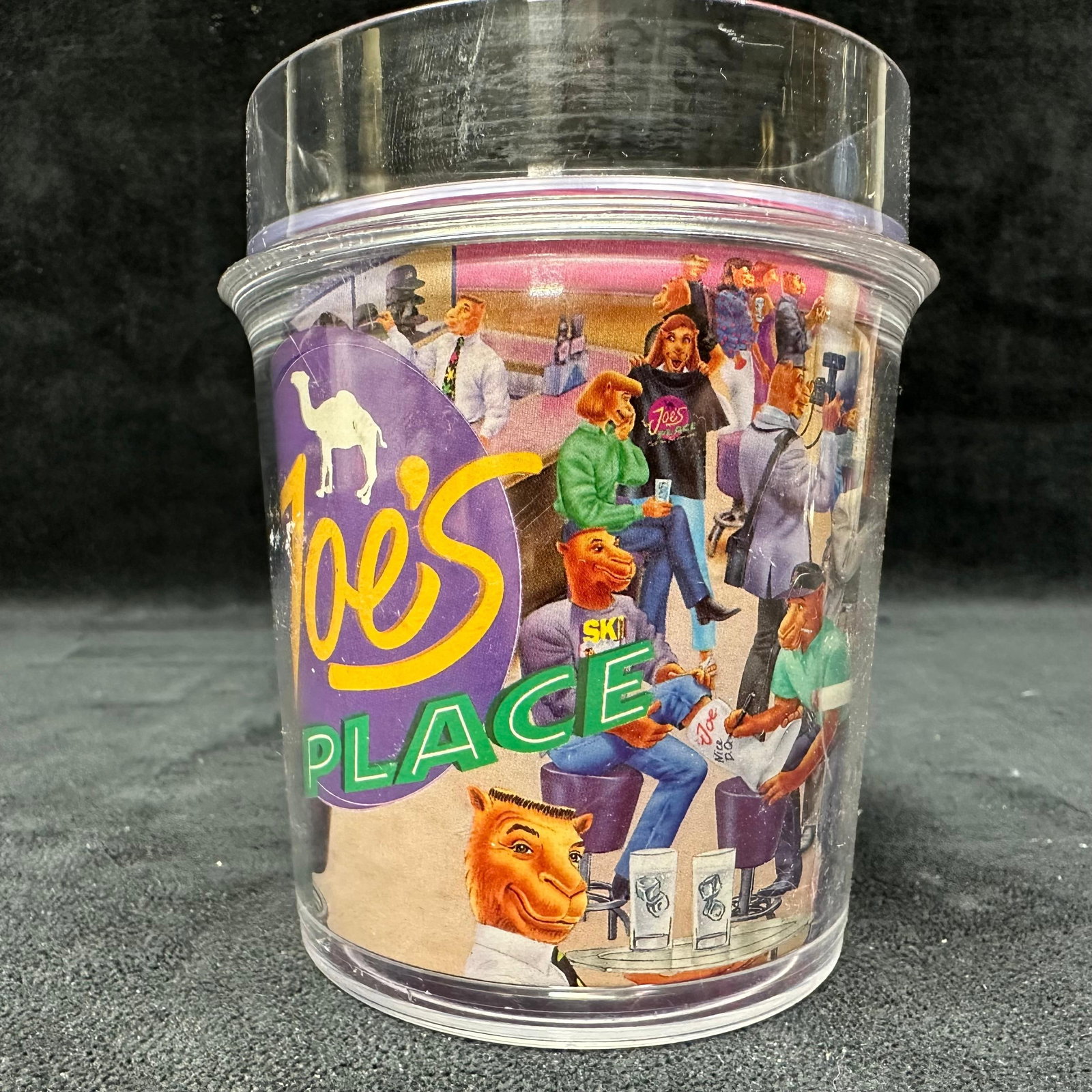 Joe's Place Camel Characters Plastic Tumbler Cup 1994: Clear plastic tumbler featuring illustrated Camel cigarette characters in a cafe scene with Joe’s Place branding. Marked 1994. Made in the USA. Vintage R. J. Reynolds Tobacco Company promotional ite