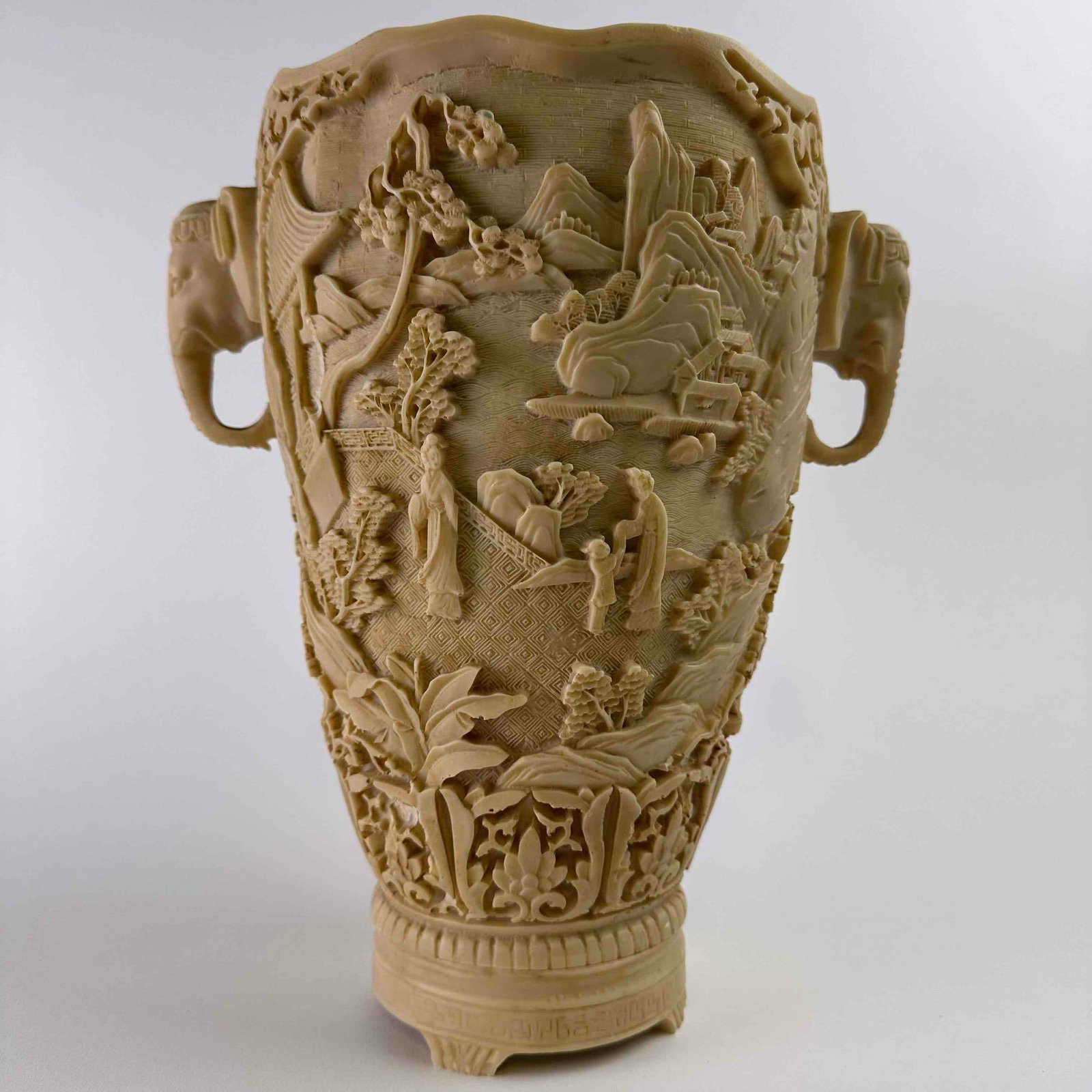 Large Chinese Faux Ivory Resin Vase Canton Carved Style Relief Elephant Head Handles: Decorative Chinese export vase in the Canton-carved style, cast in faux ivory resin with high-relief landscapes and scholar figures, pagodas, and scrolling foliage. The body is encircled by a diaper-p