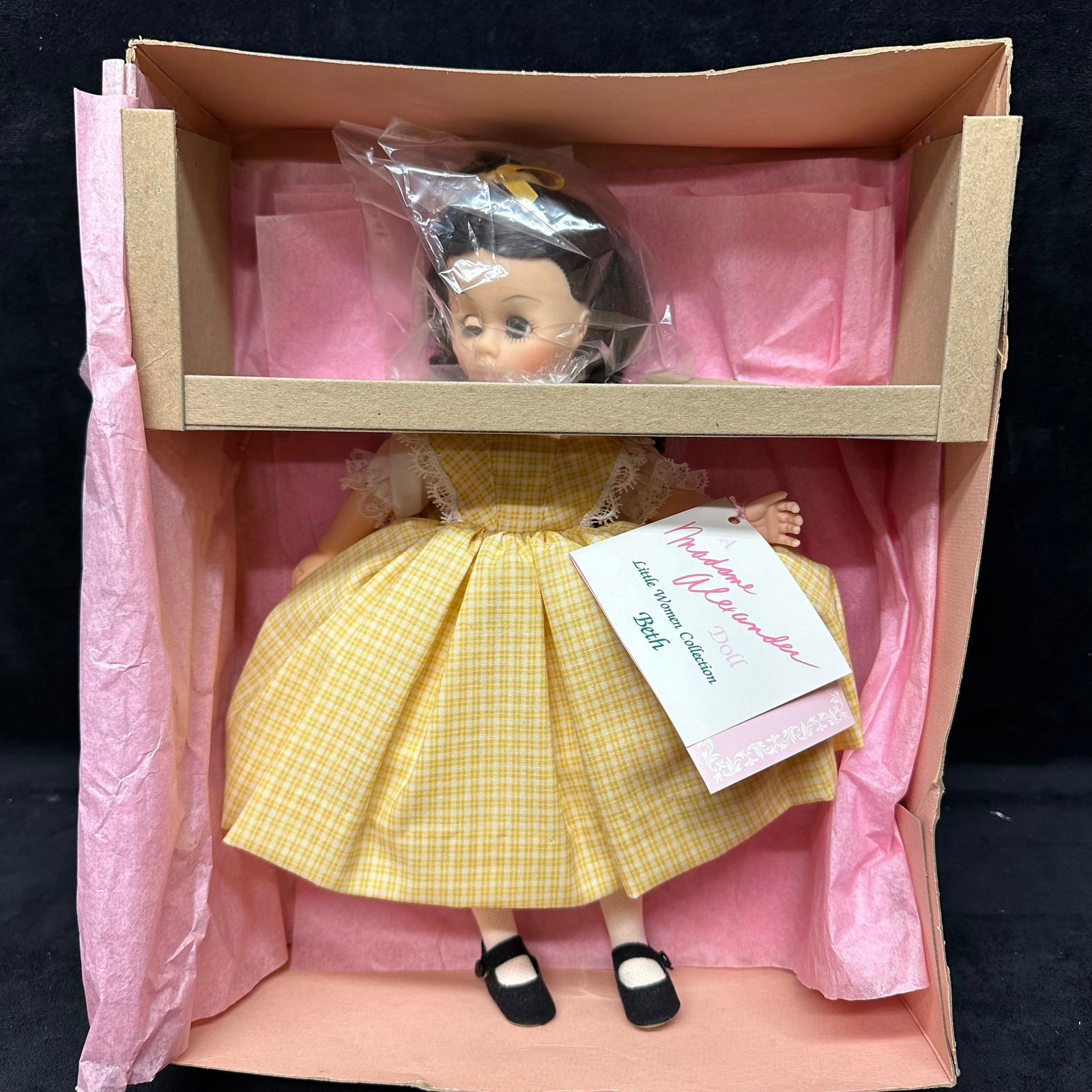 Madame Alexander Beth Doll Little Women Collection: Madame Alexander Beth doll from the Little Women Collection. She wears her original yellow gingham dress with lace trim, white stockings, and black shoes. The doll remains tied in her original box