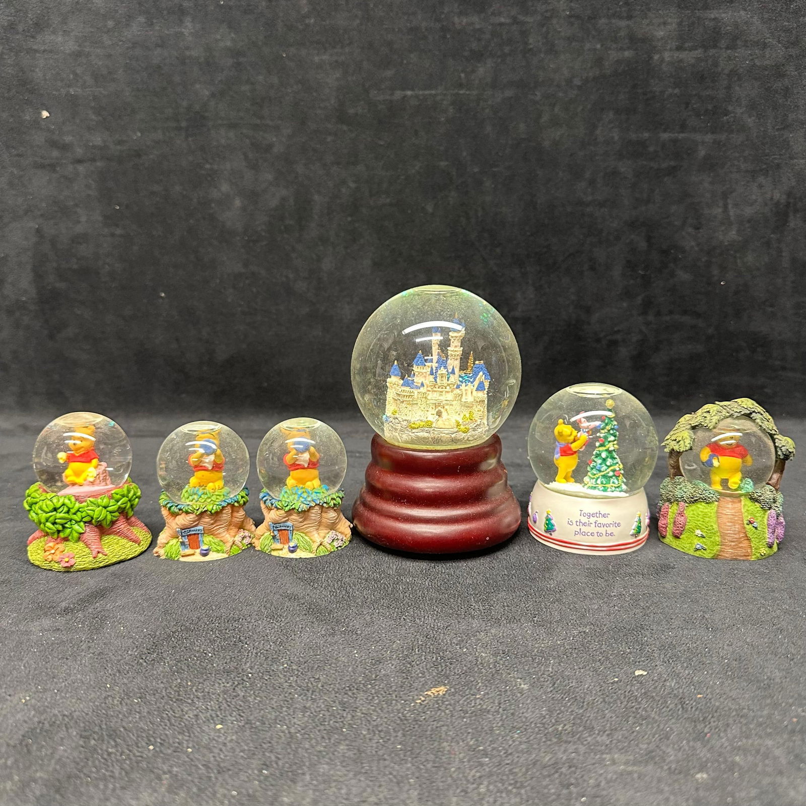 Collection of Winnie the Pooh Snow Globes Disney Cinderella Castle Collectible: Group of six decorative snow globes featuring Winnie the Pooh character scenes. Includes one larger globe depicting a Cinderella Castle on a wood-tone base and five smaller Pooh-themed globes with var