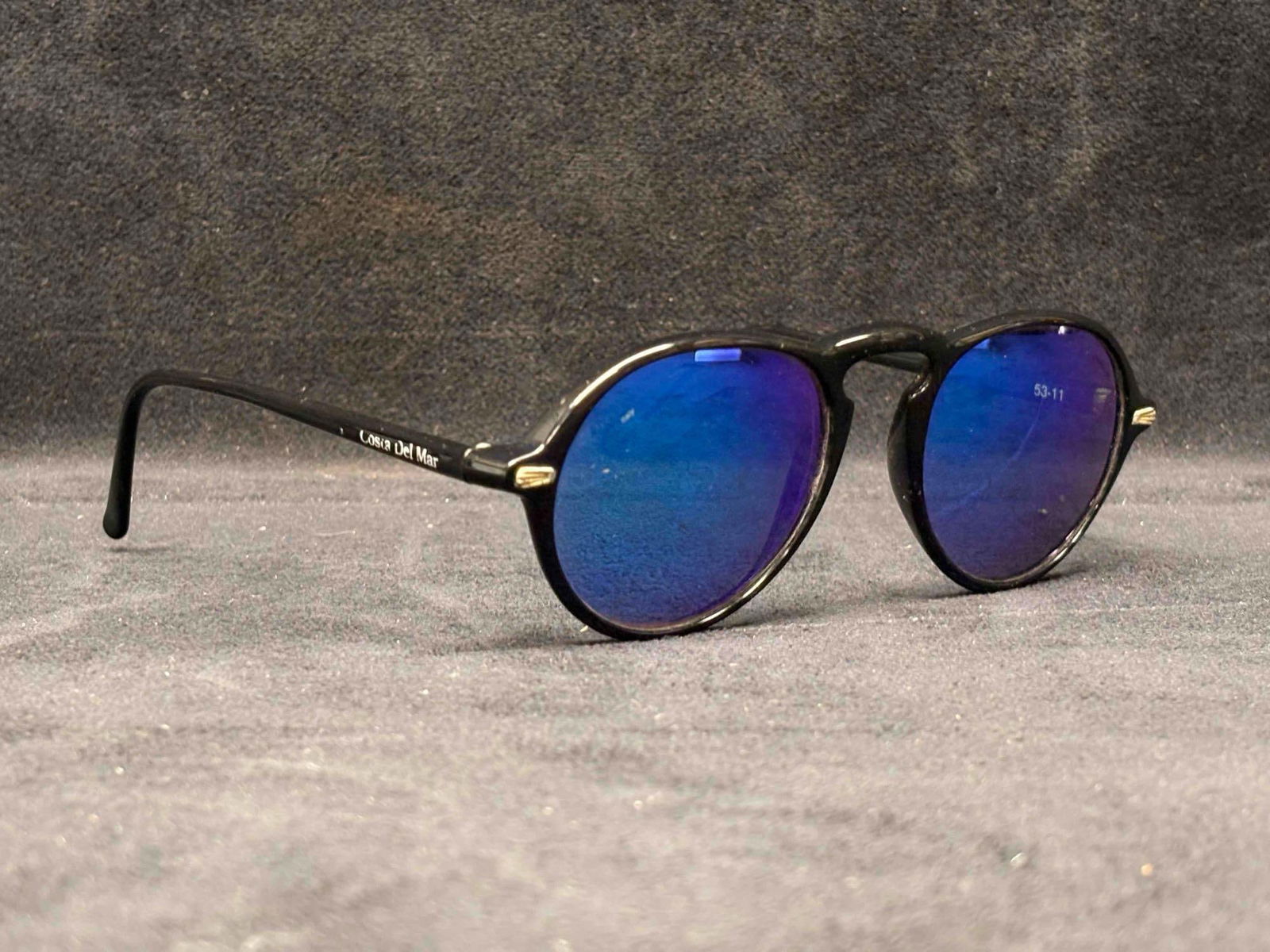 Costa Del Mar Mens Black Mirrored Sunglasses: This lot features Costa Del Mar round black frame, blue-tinted mirrored lense sunglasses. While they no longer are accompanied by their original packaging, the sunglasses themselves are in good