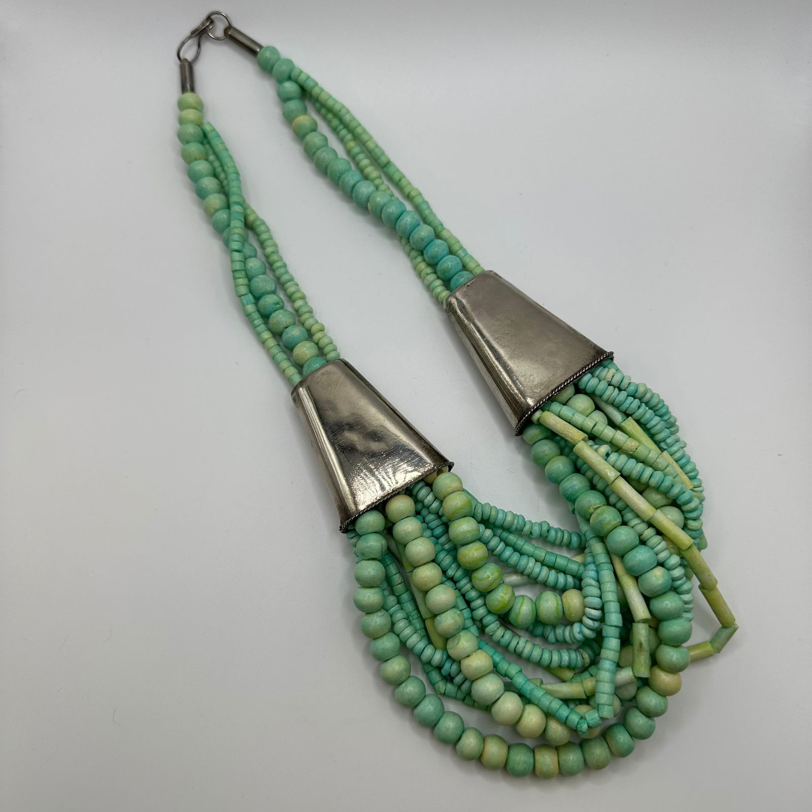 Multi Strand Beaded Necklace with Large Metal Cone Accents Turquoise Dyed Bone Shell Beads: Statement style multi-strand necklace featuring multiple strands of dyed bone/shell beads, silver-tone accents. Necklace includes multiple strands of beading with alternating dyed turquoise colored b