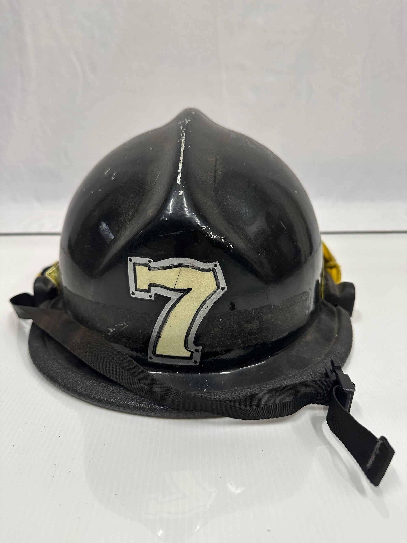 Cairns and Brother Style Black Safeco Firefighter Helmet R184: Vintage firefighter helmet with traditional hard plastic leather-style black shell and raised ridge top. The helmet displays the number “7” on the front and “421” on the rear in painte