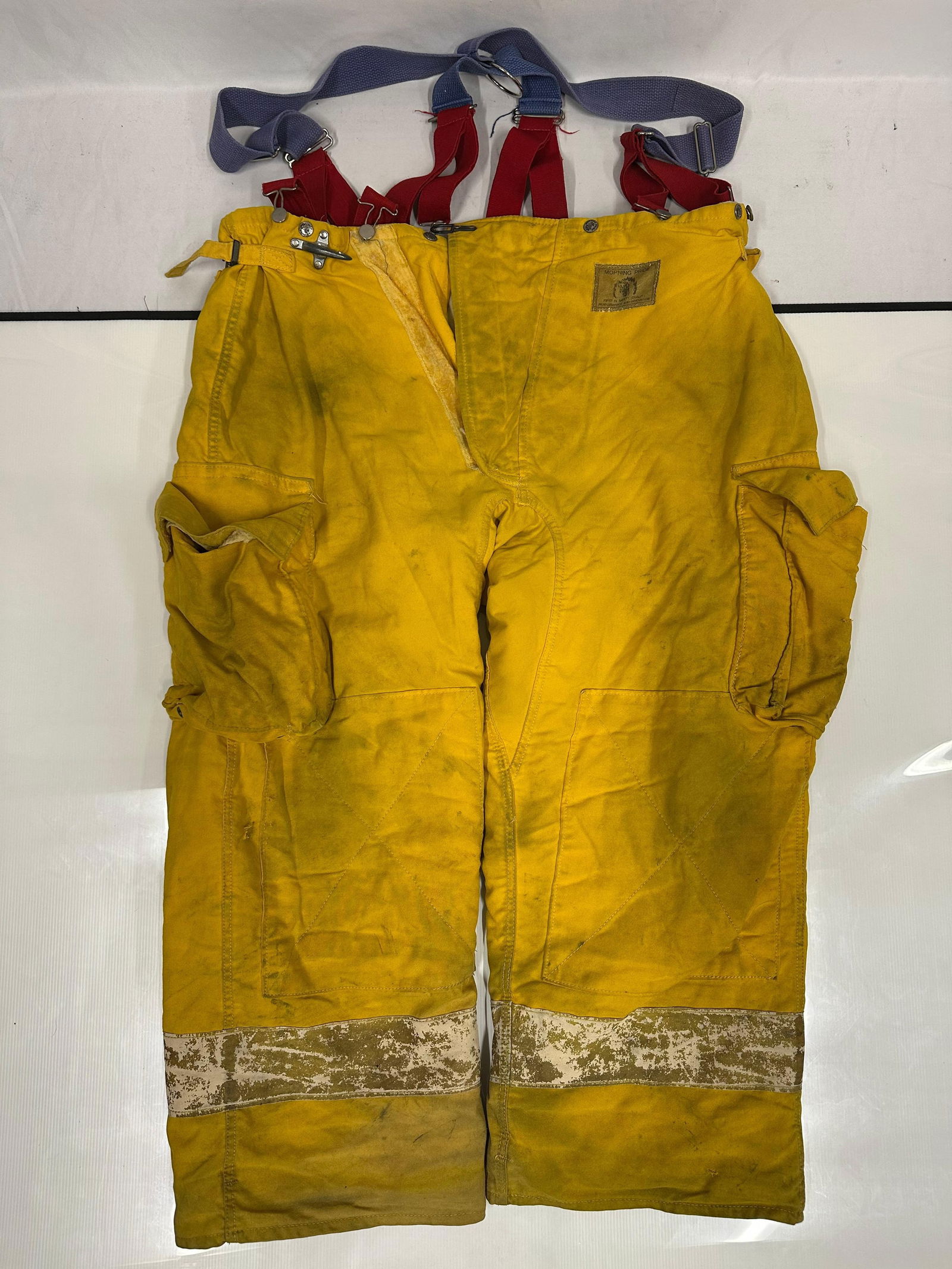 Morning Pride Firefighter Turnout Pants Yellow Bunker Pants with Suspenders: Yellow firefighter turnout bunker pants made by Morning Pride. Heavy-duty fire-resistant construction with cargo pockets, reinforced knees, and reflective striping near the lower legs. Includes red