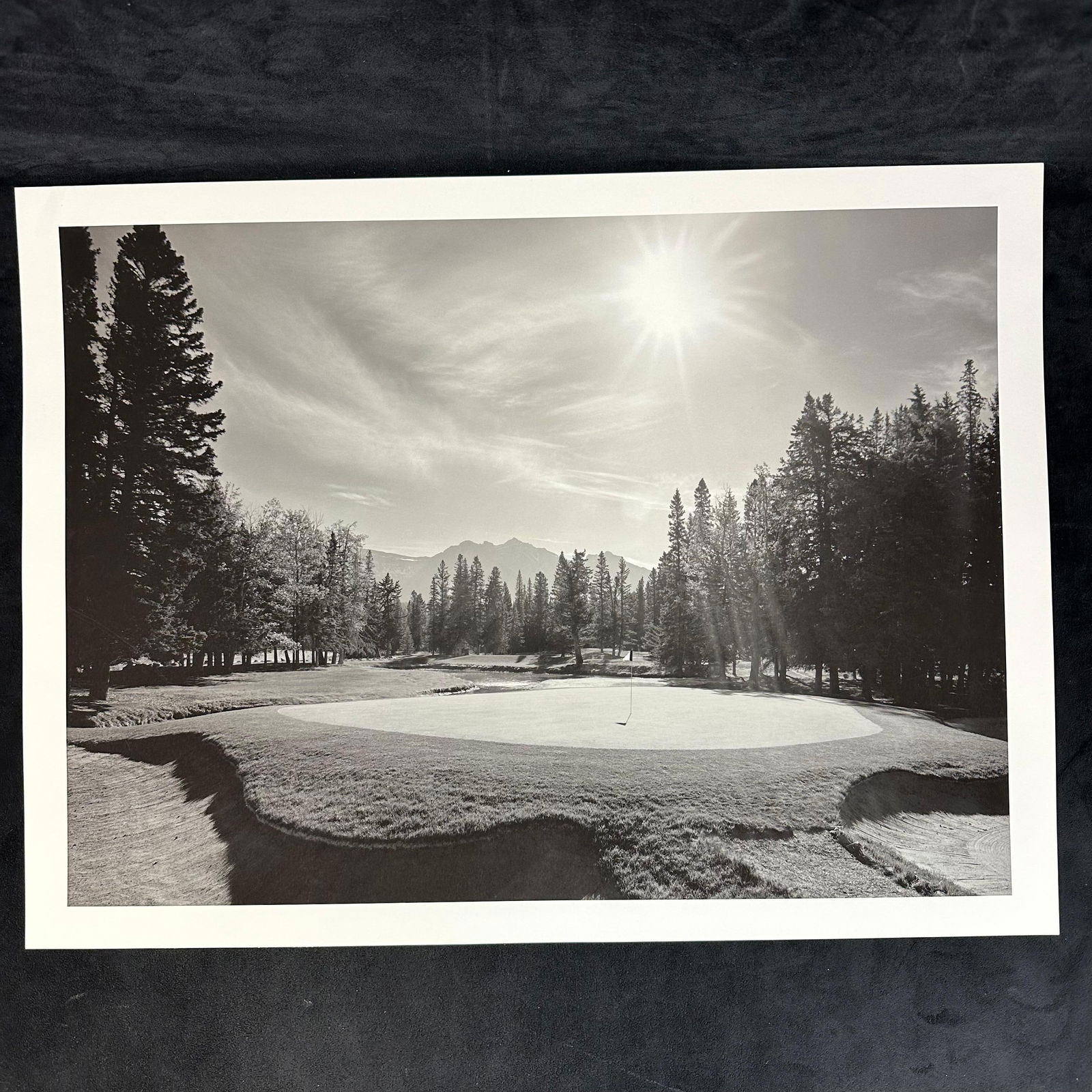 Black and White Inkjet Photography Print Golf Course with Mountain View and Sunburst: Black and white ink jet photographic print depicting a golf course green surrounded by tall trees, with a dramatic sunburst effect overhead and mountains visible in the distance. The composition highl