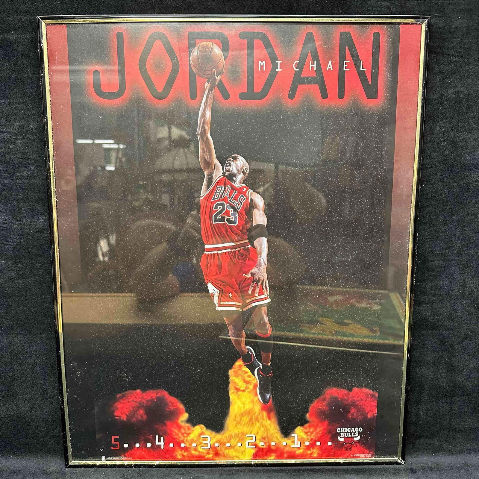 Michael Jordan Chicago Bulls NBA 1996 Framed Poster: 54321 NBA Chicago Bulls Michael Jordan 1996 poster featuring Jordan dunking. The plastic frame is black with a gold trim. Frame shows signs of wear, with some gold trim peeling. This item is in good p