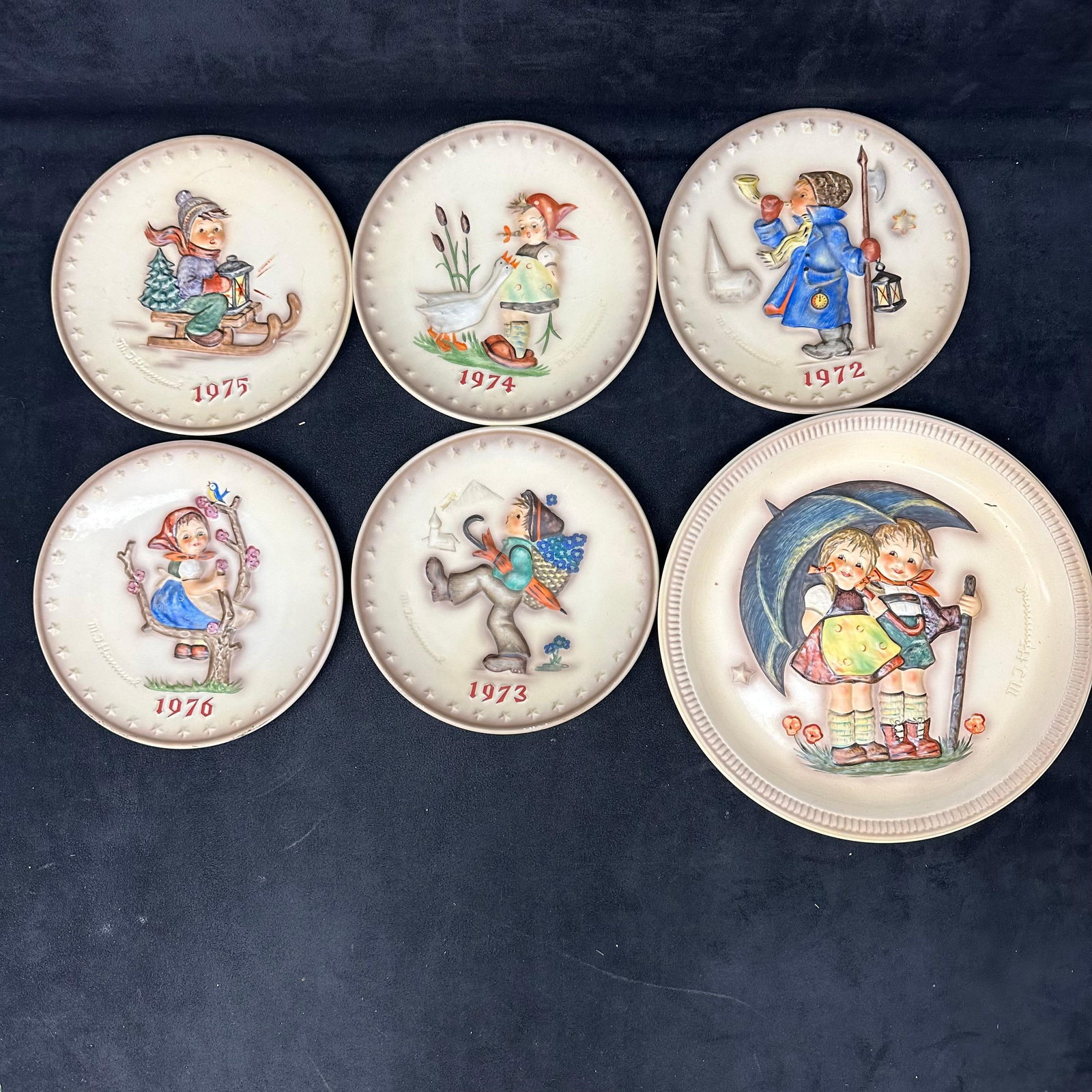 Set of 6 M.J. Hummel Annual Collector Plates 1972-1976 by Goebel W. Germany: Collection of M.J. Hummel annual collector plates produced by Goebel, West Germany. Each plate is hand-painted and features classic relief designs of children in pastoral scenes, signed “M.I. Hummel