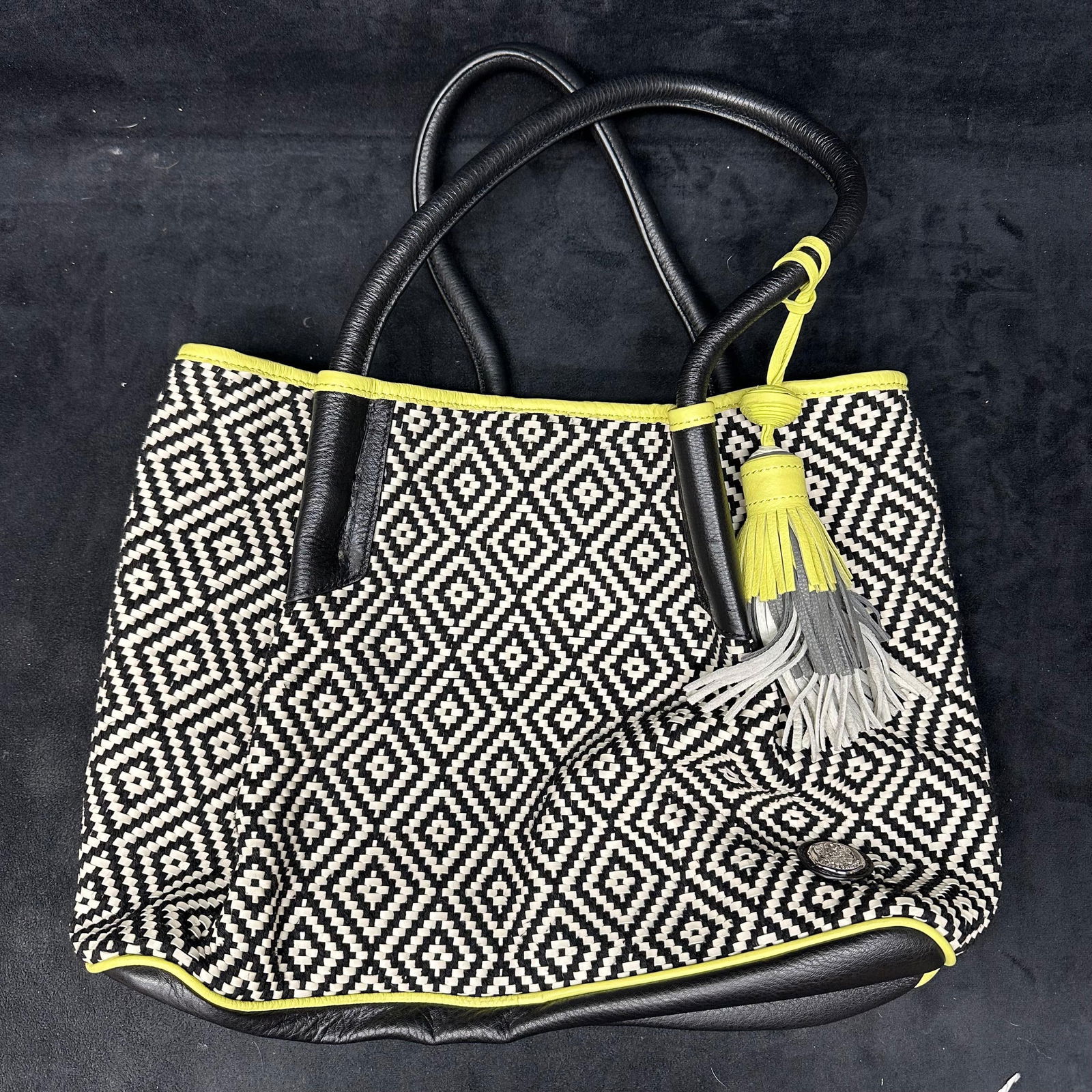 Vince Camuto Woven Tote Handbag Black and White with Light Green Trim: Vince Camuto woven tote handbag featuring a black and white geometric pattern with black leather handles and trim. Accented with lime green piping and tassel detail. Open top with black fabric interio
