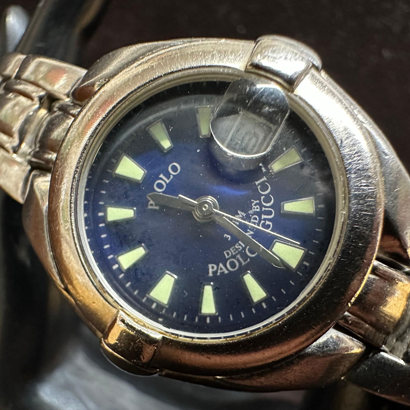 Paolo Gucci Stainless Steel Wristwatch Blue Dial: Paolo Gucci wristwatch featuring a blue dial with luminous hour markers and a date window with a magnifier. Stainless steel case and bracelet. Case back marked base metal bezel, stainless steel back,