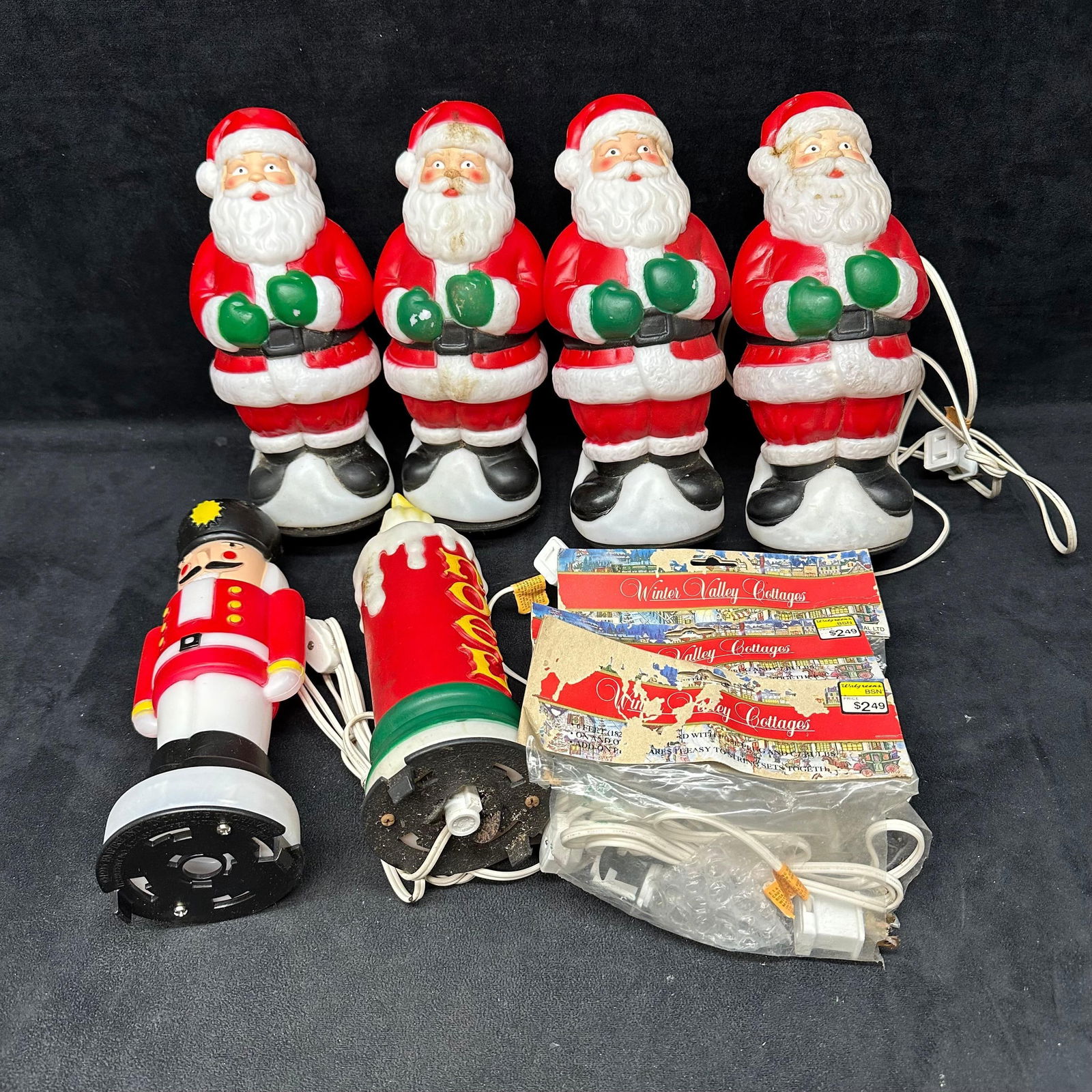 Group of Holiday Christmas Blow Mold Decorations with Santa Figures: Group of vintage plastic Christmas light-up decorations including four Santa Claus blow mold figures, a toy soldier figure, and a Noel candle decoration. Also includes three packaged light cords label