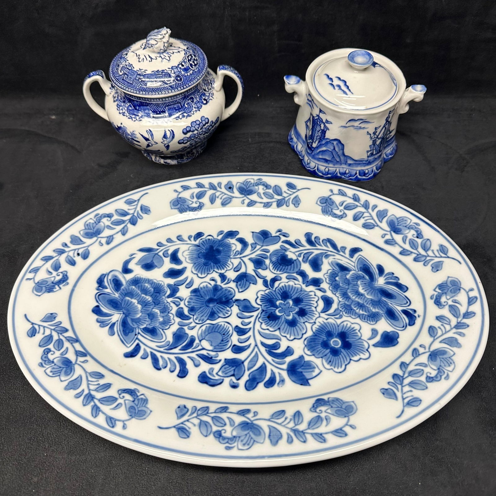 Blue and White Porcelain Serving Lot Platter Sugar Bowl and Covered Jar: Decorative blue and white porcelain serving lot consisting of three pieces. Includes one oval floral serving platter with scrolling flower and vine decoration, one lidded sugar bowl with dual handles