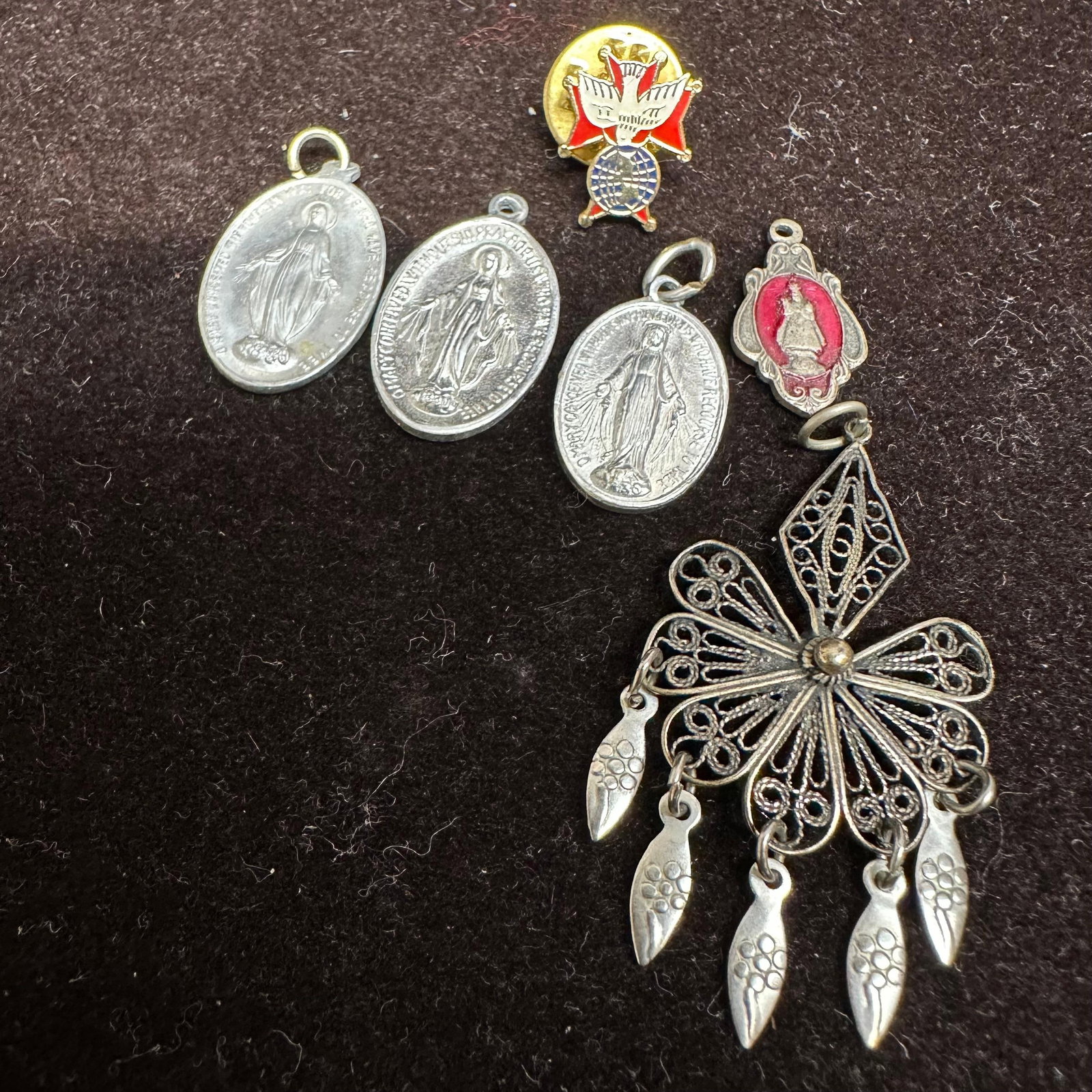 Group of Religious Medals Lapel Pin and Filigree Pendant Set: Collection of religious items, including three Miraculous Mary medals, one Infant of Prague medal, one enameled red and gold religious pin, and a large filigree pendant with dangling teardrop