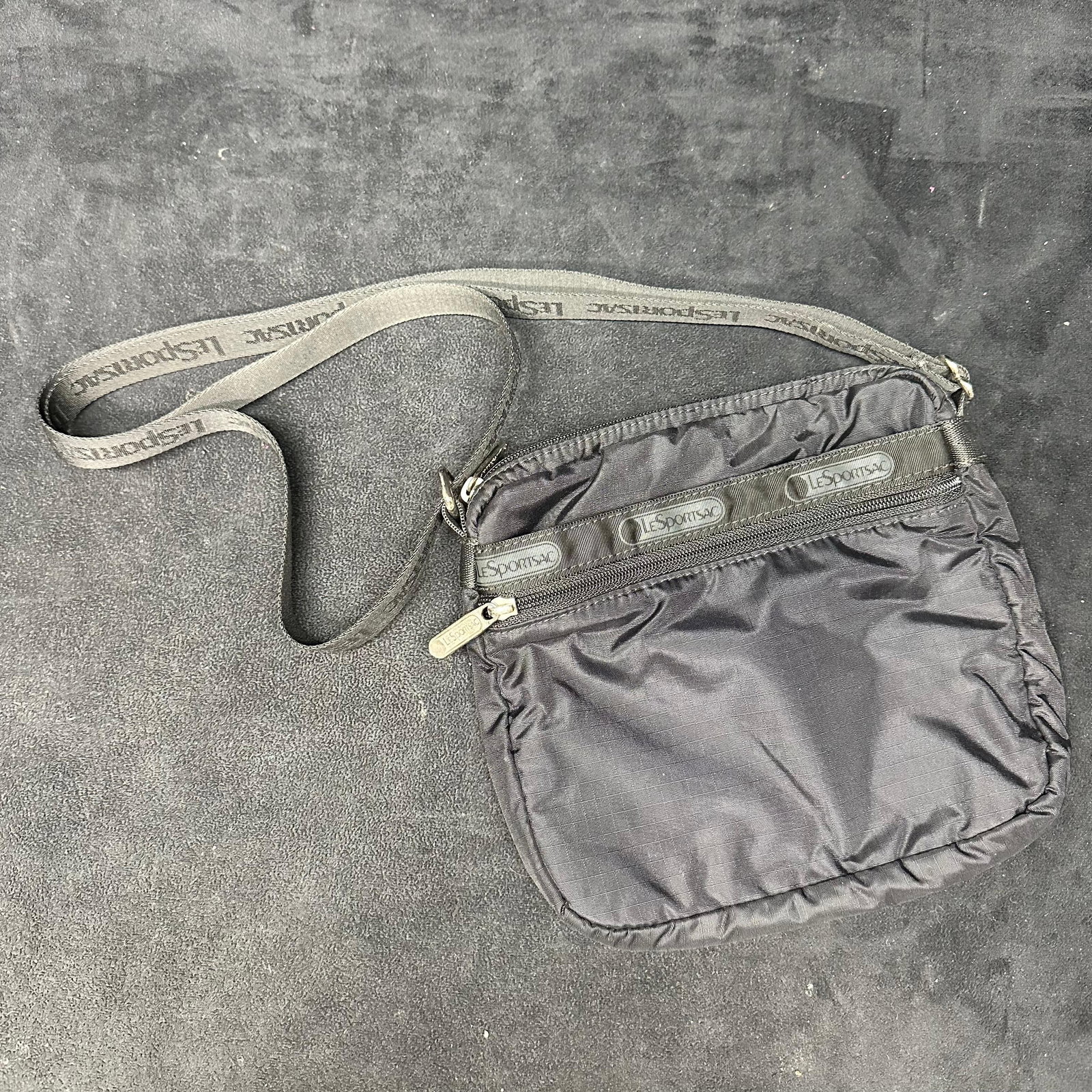 LeSportsac Black Nylon Crossbody Shoulder Bag: Used a LeSportsac black nylon crossbody bag with an adjustable logo strap. Features zip-top closure, exterior zip pocket, and lightweight nylon construction. Shows light signs of wear consistent with