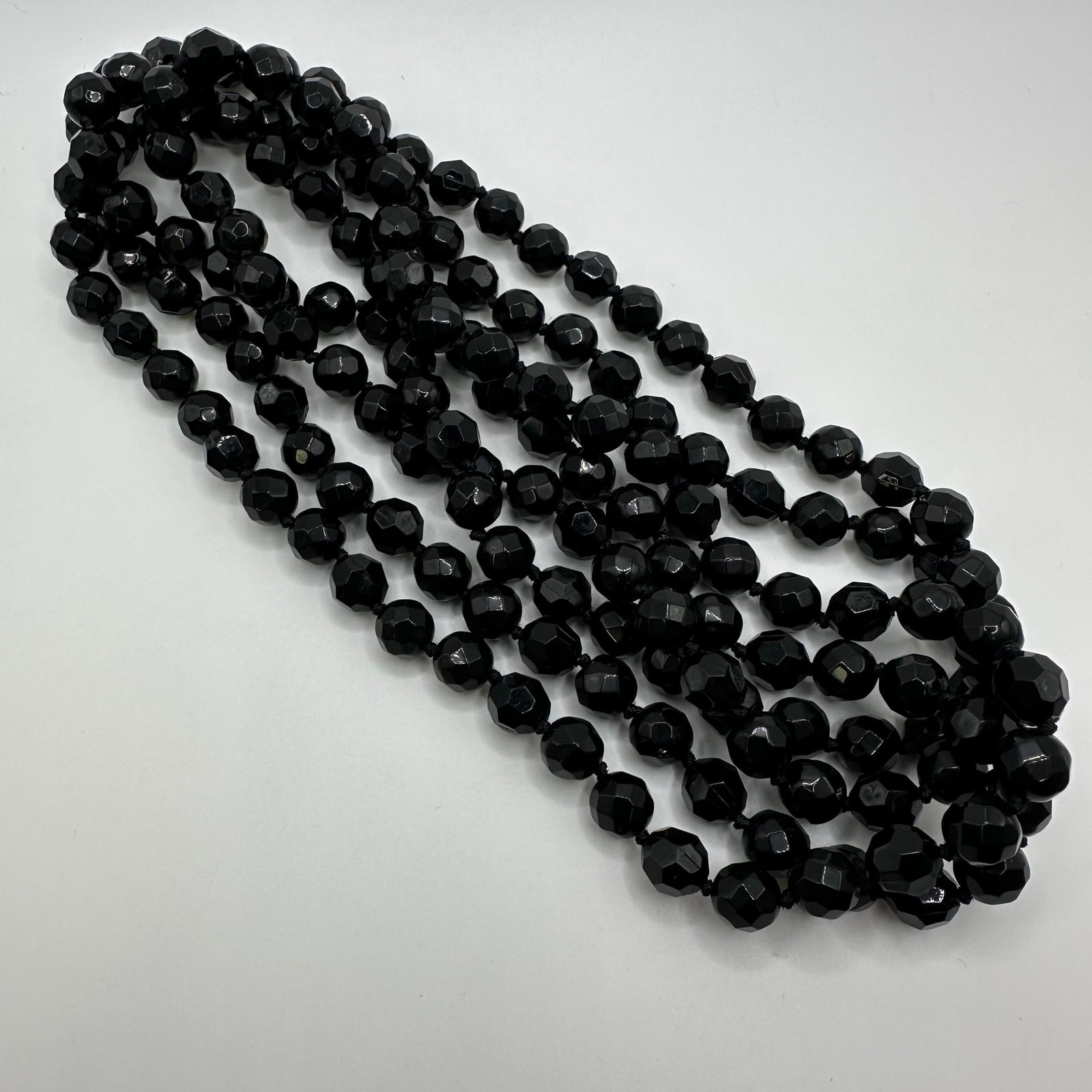 Large Long Blass Glass Faceted Round Beaded Necklace: Long, large single-strand black glass beaded necklace. No hallmarks. This item is in good pre-owned, previously used/displayed condition with noticeable light wear and surface scratches. Please