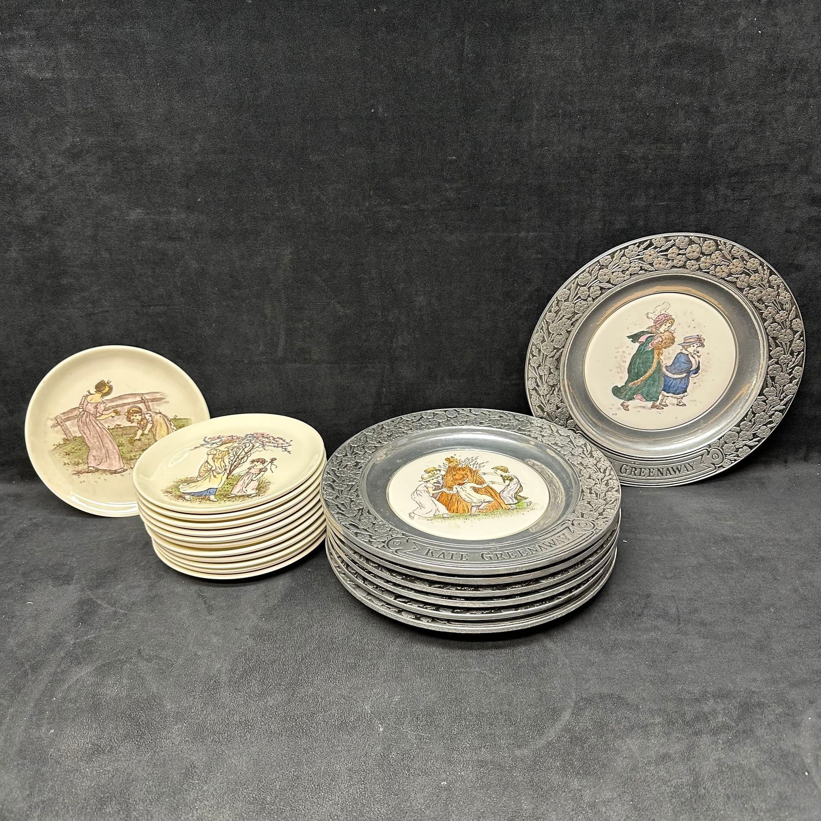 Collection of Kate Greenaway Decorative Plates Pewter and Porcelain Mix: An assortment of vintage decorative plates featuring charming Kate Greenaway illustrations, inspired by the 19th-century English artist known for her idyllic depictions of childhood and pastoral life.