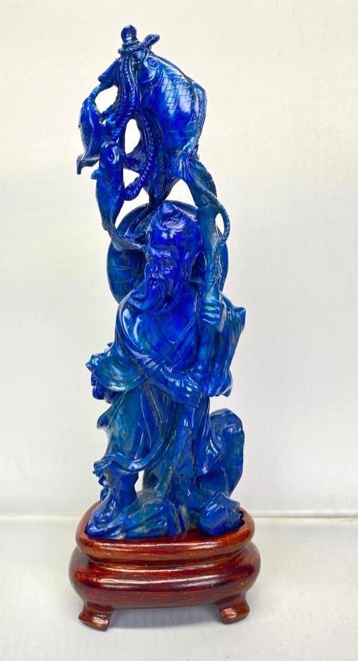 Lapis Lazuli Chinese Fisherman Figurine: Lapis Lazuli Chinese Fisherman Figurine Figure of a man holding several fish on a pole in Lapis Lazuli, with a wooden base. The top appears to have been repaired, but the figure is otherwise in good