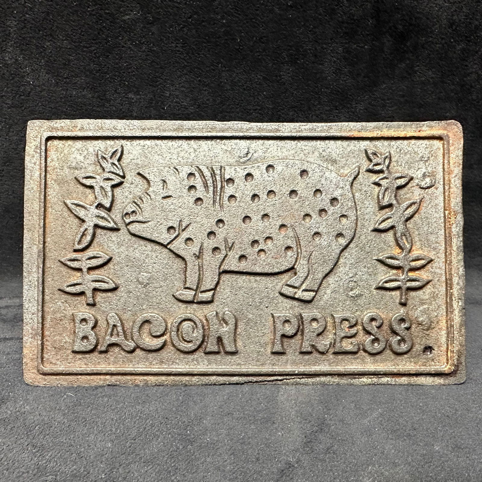 Cast Iron Vintage Bacon Press with Pig Motif Wooden Handle: Vintage cast iron bacon press featuring a raised pig design with Bacon Press text and decorative foliage accents. Rectangular cast iron plate with integrated wooden handle secured by metal brackets. E