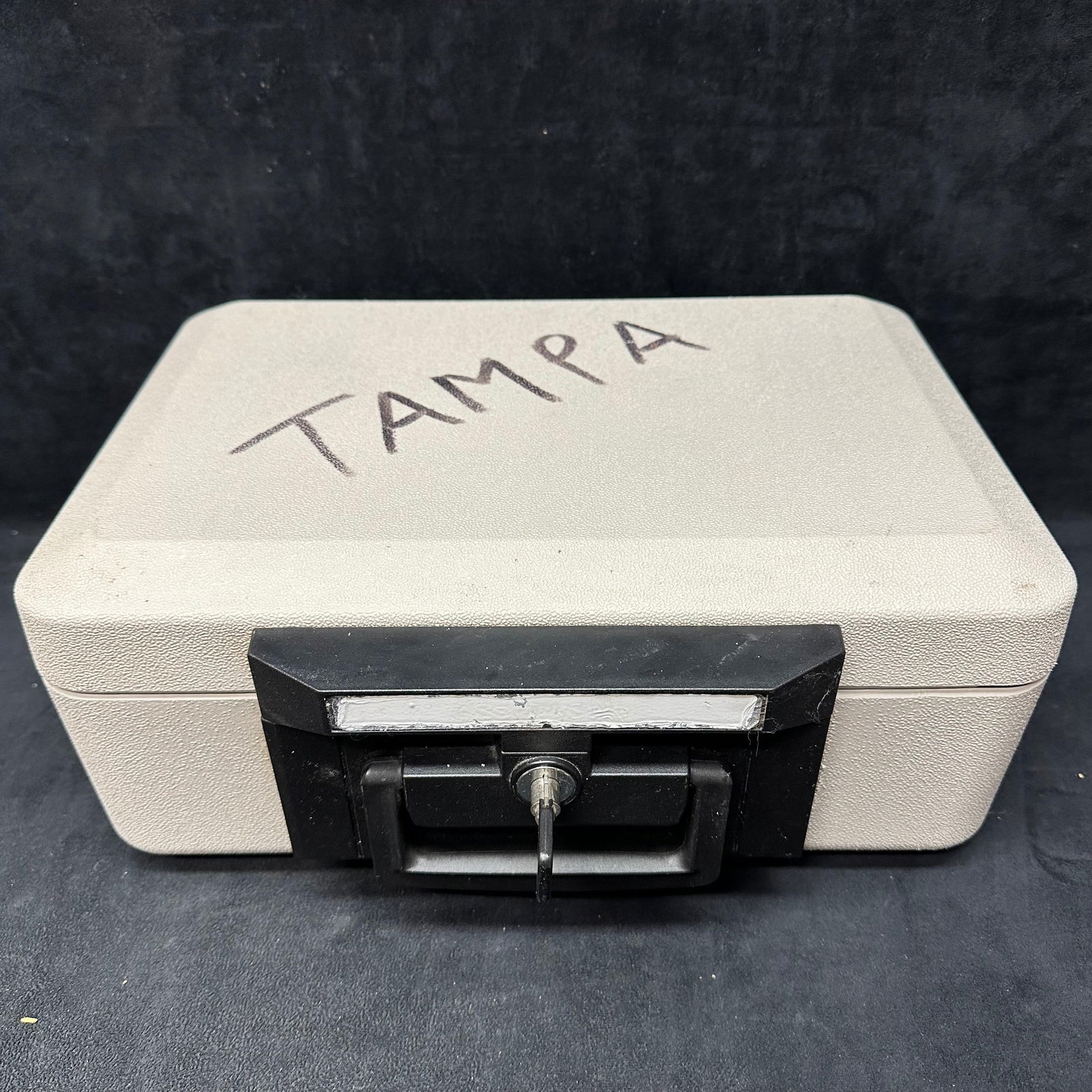 Sentry Safe Portable Locking Cash Box with Key Beige Hard Case: Portable hard-sided cash box featuring a beige textured exterior with a black handle and front lock. Includes a working keyed lock key present. Hinged lid opens to an empty interior compartment