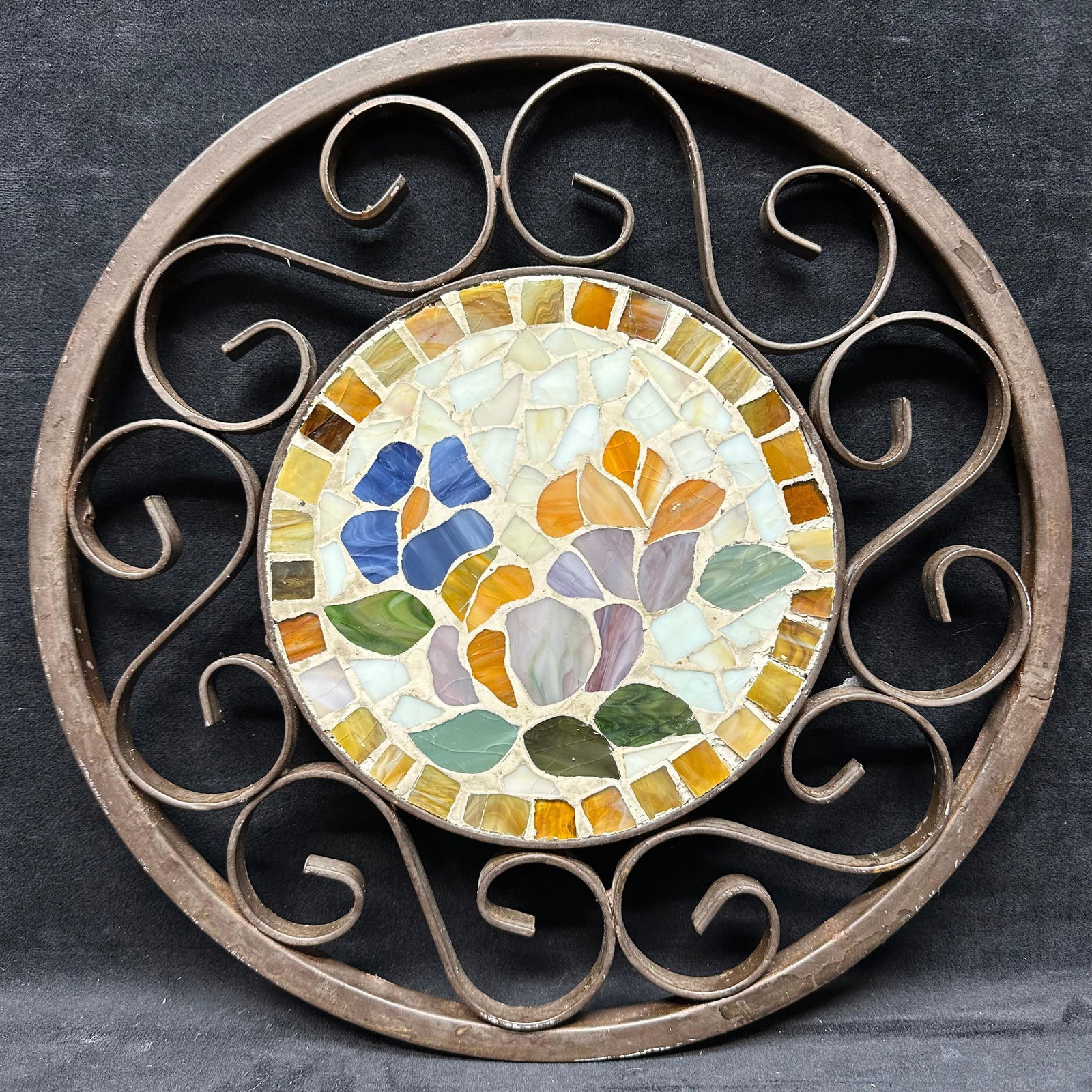 Glass Mosaic Floral Wall Hanging with Metal Frame: Circular decorative wall hanging featuring a colorful mosaic floral motif crafted from glass pieces in shades of blue, orange, purple, green, and amber. The mosaic is set in a heavy scrolled metal fra